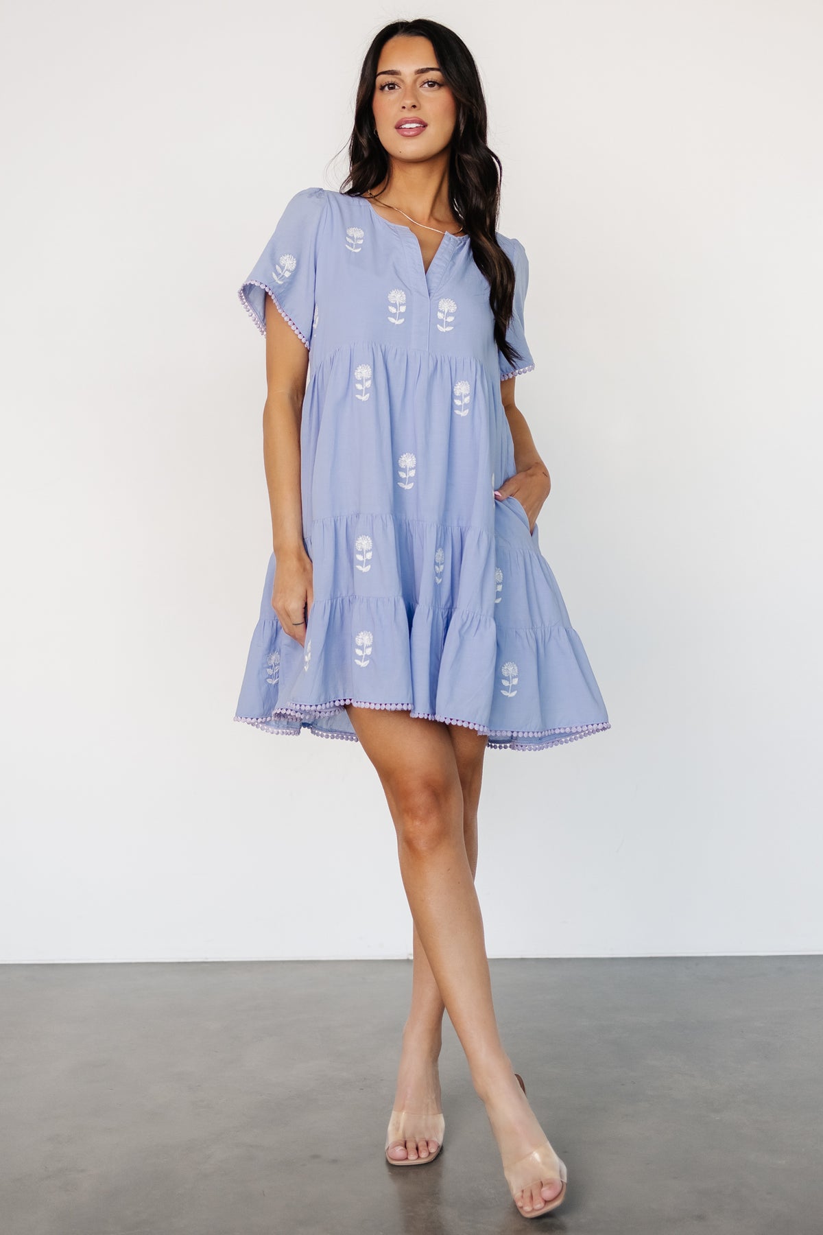 Styled outfit image: ivory embroidered short dress paired with sandals, showing movement and casual warm-weather styling.