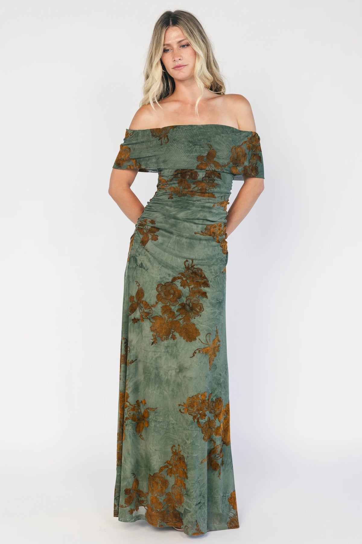 Model wearing an off-the-shoulder maxi dress with a green mesh overlay and copper velvet floral detailing.