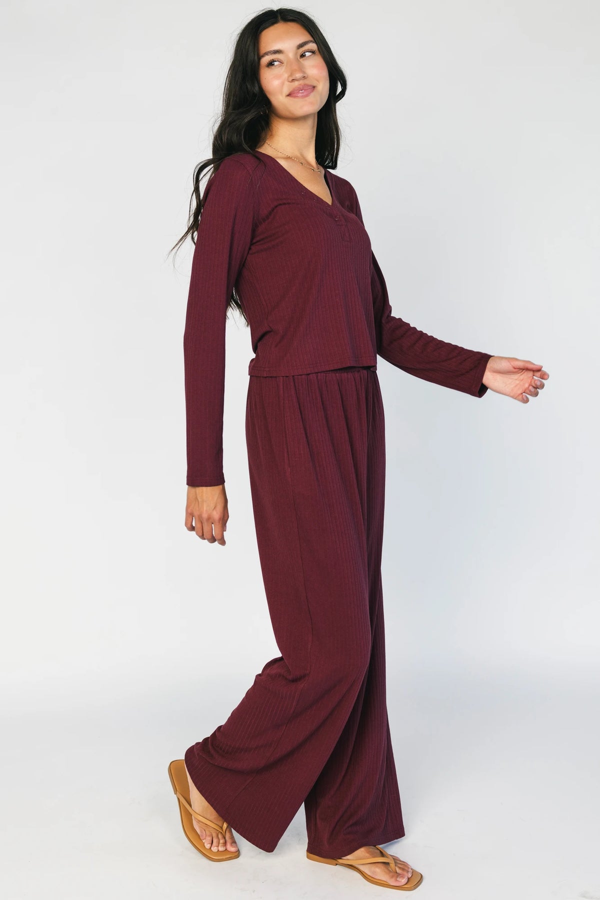 Model wearing the Rubi Soft Ribbed Pajama Set in Burgundy featuring a soft ribbed knit, long-sleeve V-neck top with a snap-button placket, and matching straight-leg pants with an elastic waistband and side pockets.