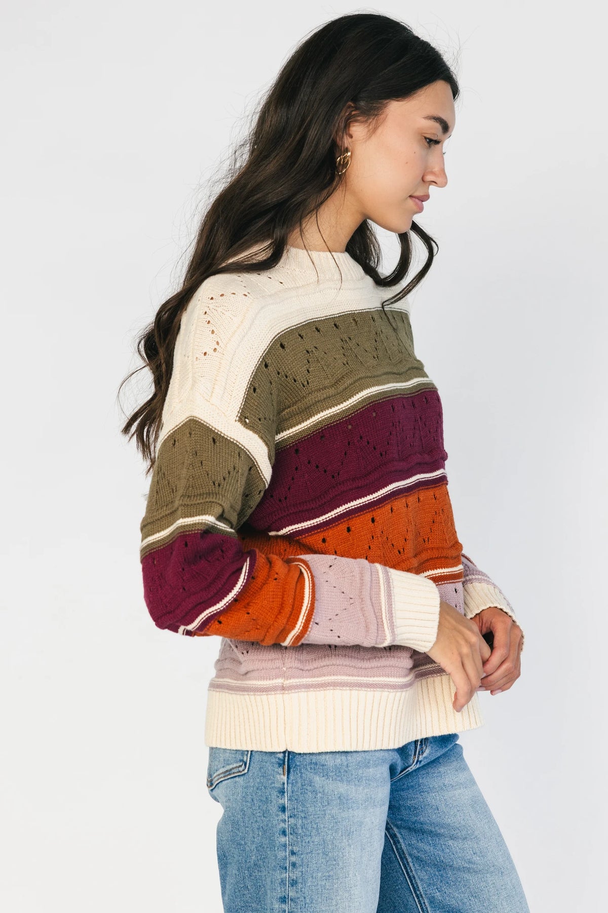 Ivory striped sweater with green, mulberry, rust, and purple horizontal stripes, a round neckline, dropped shoulders, long sleeves, and a relaxed fit.