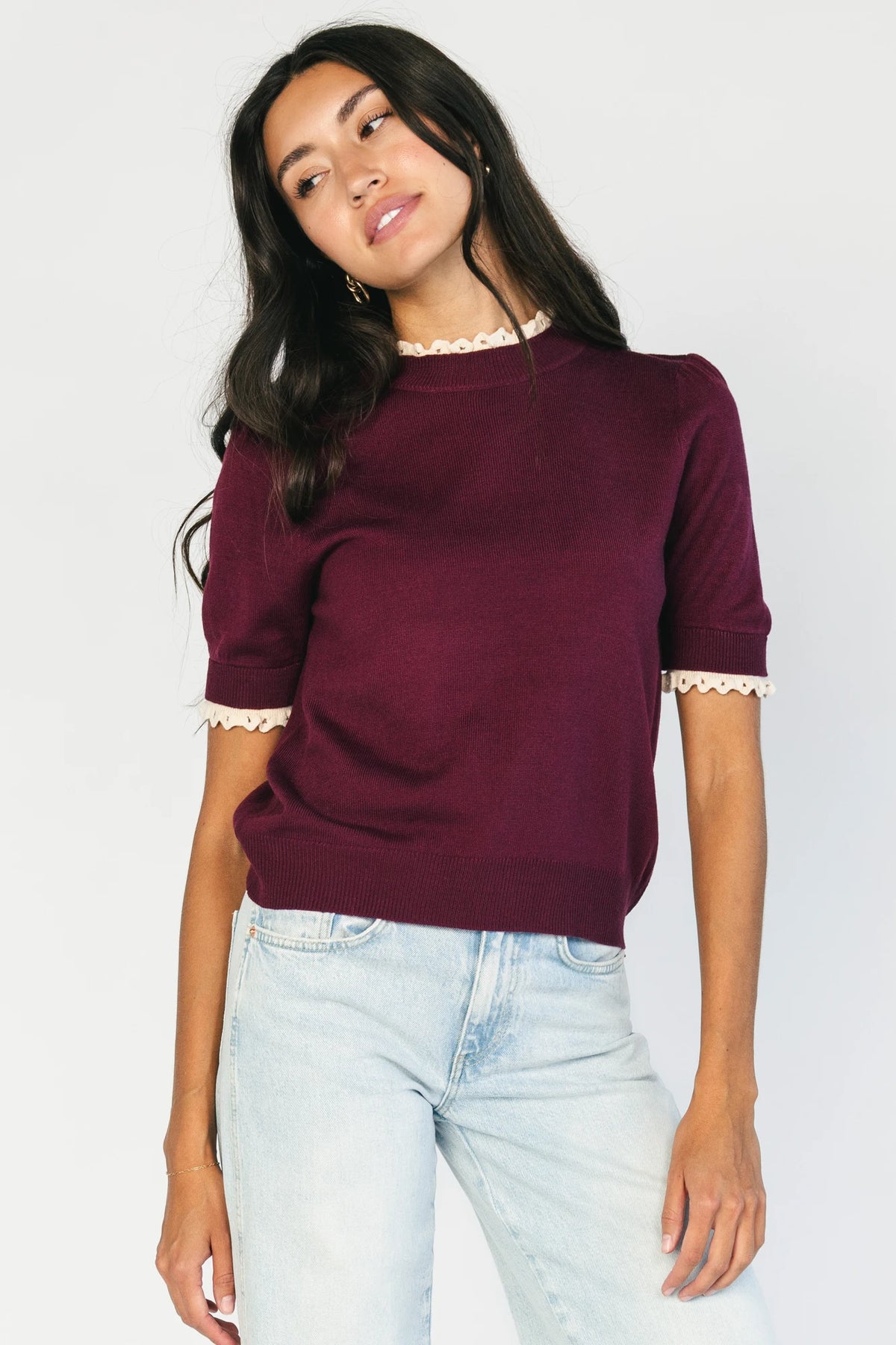 Model wearing the Adeline Sweater Top in Wine featuring a mock neckline, short sleeves with gathered shoulders, contrast ivory eyelet ruffle trim at the neckline and cuffs, and a classic fitted knit silhouette.