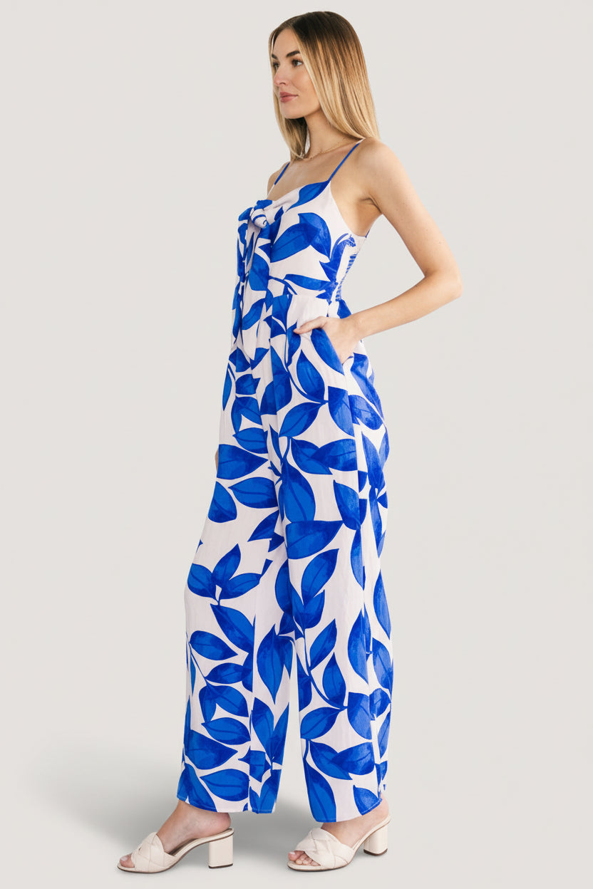Styled outfit shot: Noémie Jumpsuit in cobalt leaf print paired with casual sandals, showing full-length straight leg silhouette.