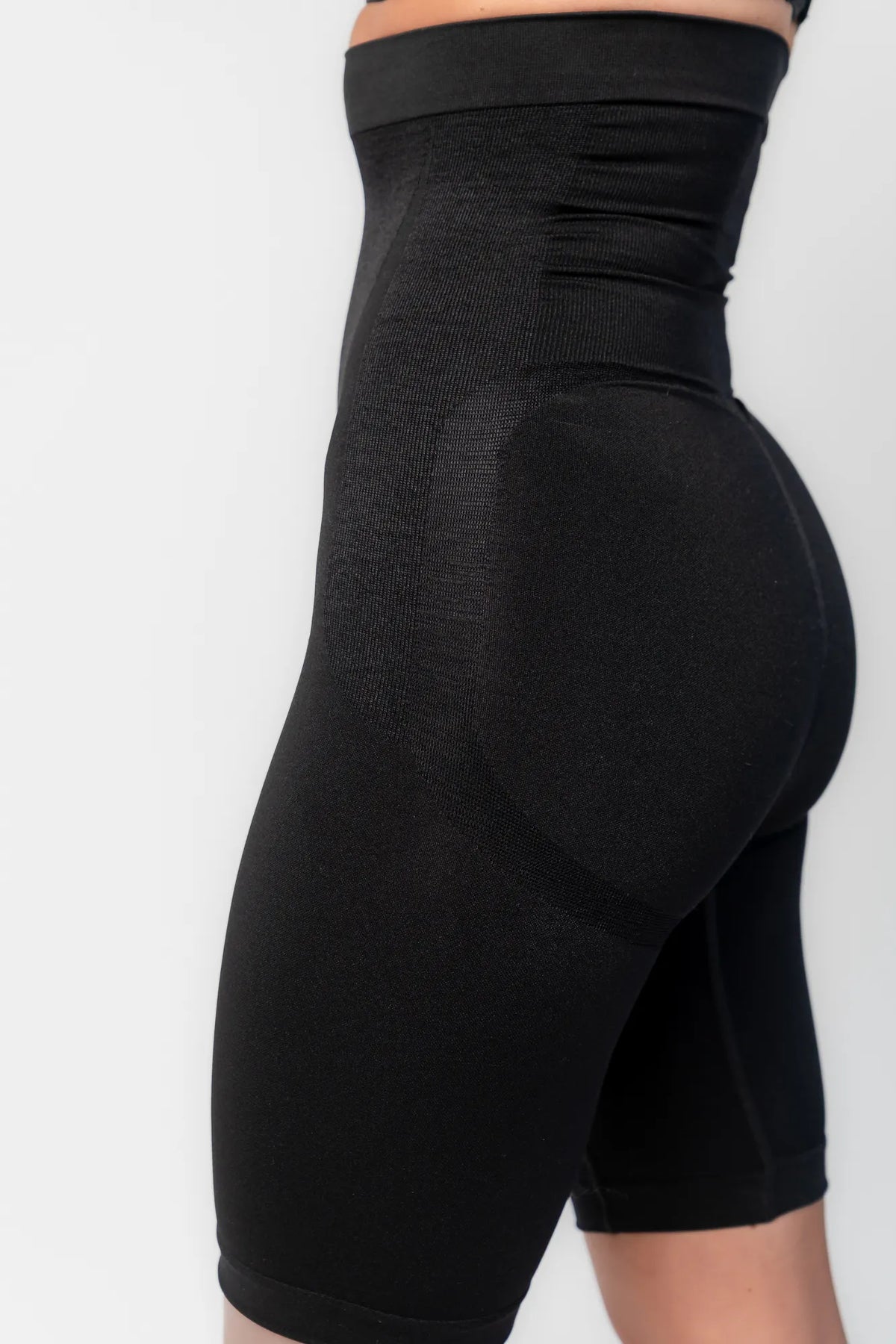 Model wearing black high-waisted shaping shorts with a seamless design and mid-thigh length.