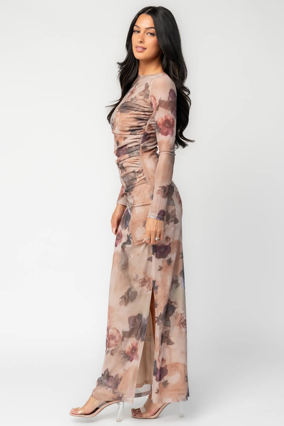 Model wearing a dark taupe floral maxi dress with a fitted bodycon silhouette, sheer long sleeves, and a round neckline.