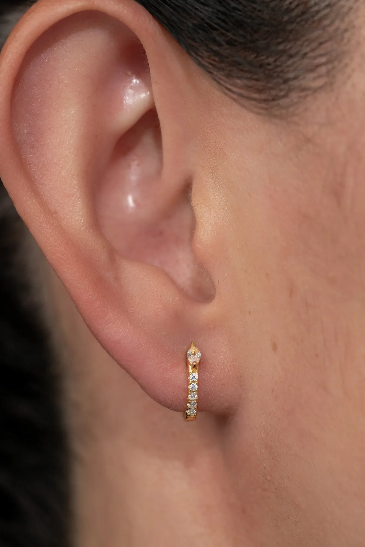 Model wearing petite gold huggie hoop earrings featuring a marquise-cut crystal accent and a row of sparkling stones along the front.