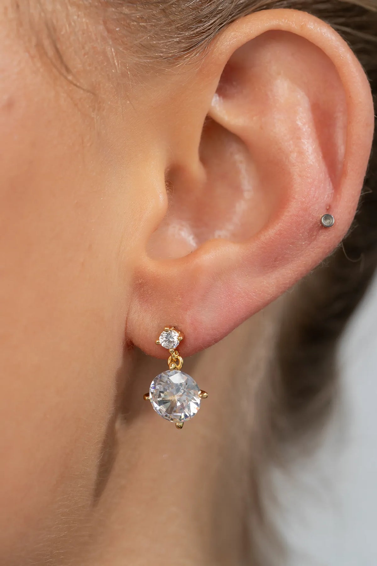 Model wearing gold-tone drop earrings featuring sparkling round zircon stones suspended from petite stud tops.