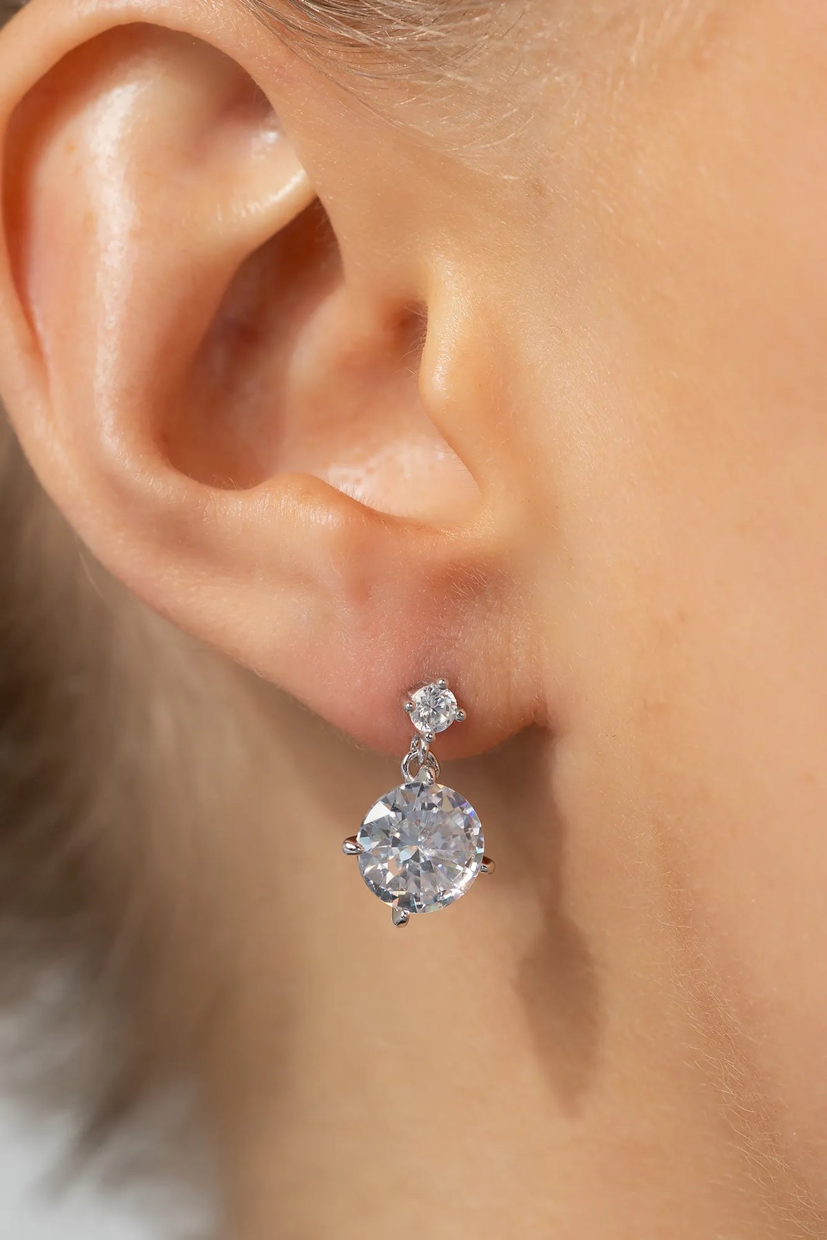 Model wearing silver-tone drop earrings featuring sparkling round zircon stones suspended from petite stud tops.