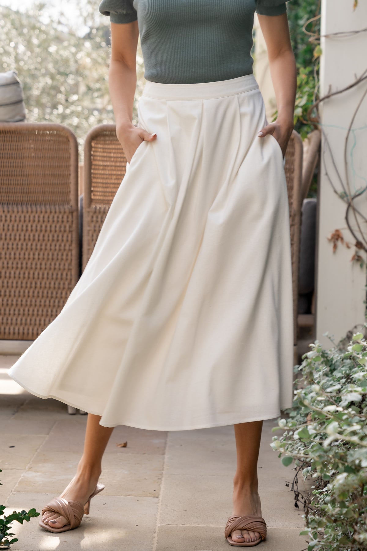Model wearing off-white pleated midi skirt, front view showing high-rise waistband, flowing pleats, and subtle fabric texture across the skirt.