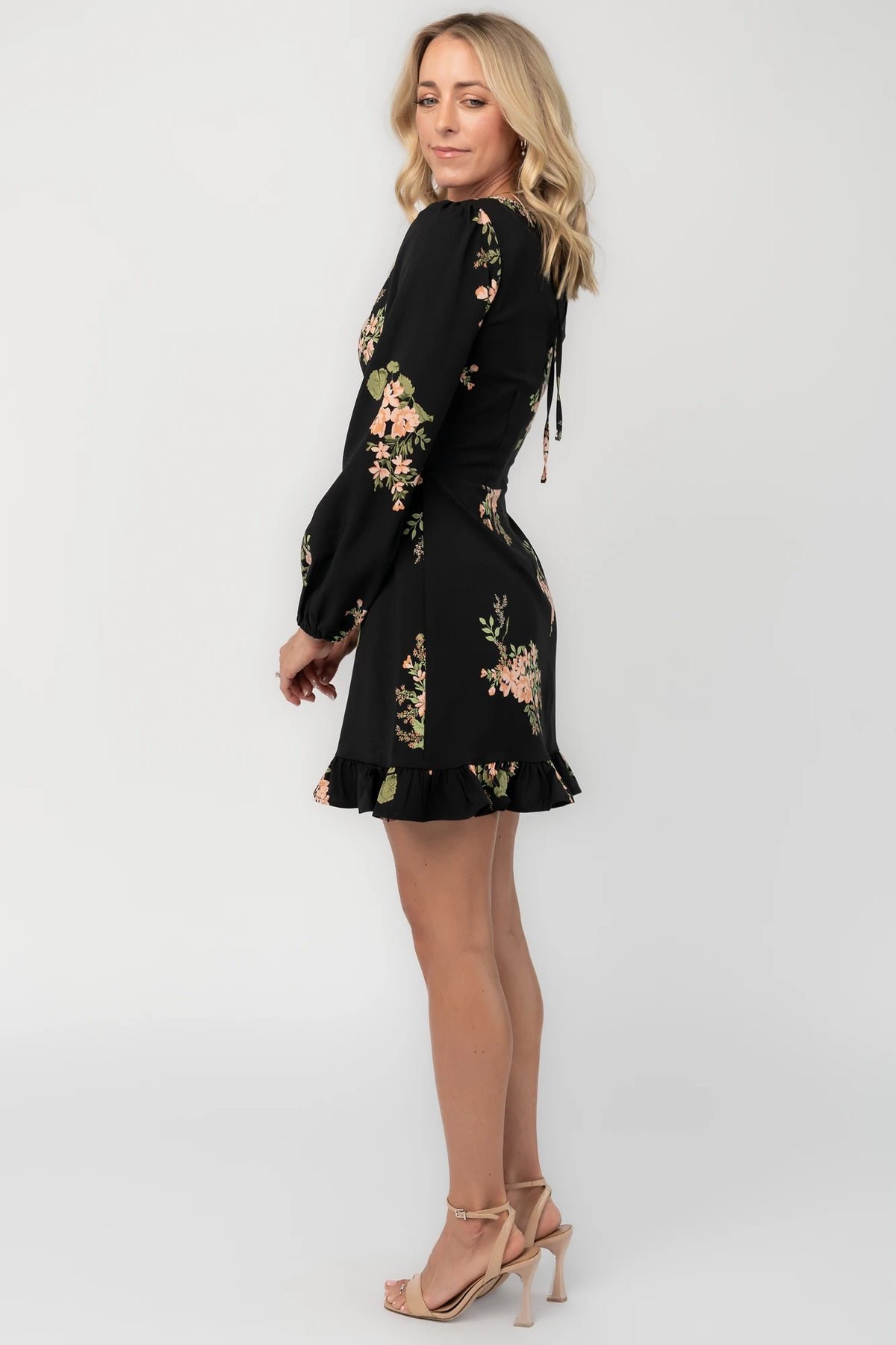 Black floral mini dress with a round neckline, long sleeves, fitted bodice, ruffle hem, back keyhole tie, and hidden back zipper.