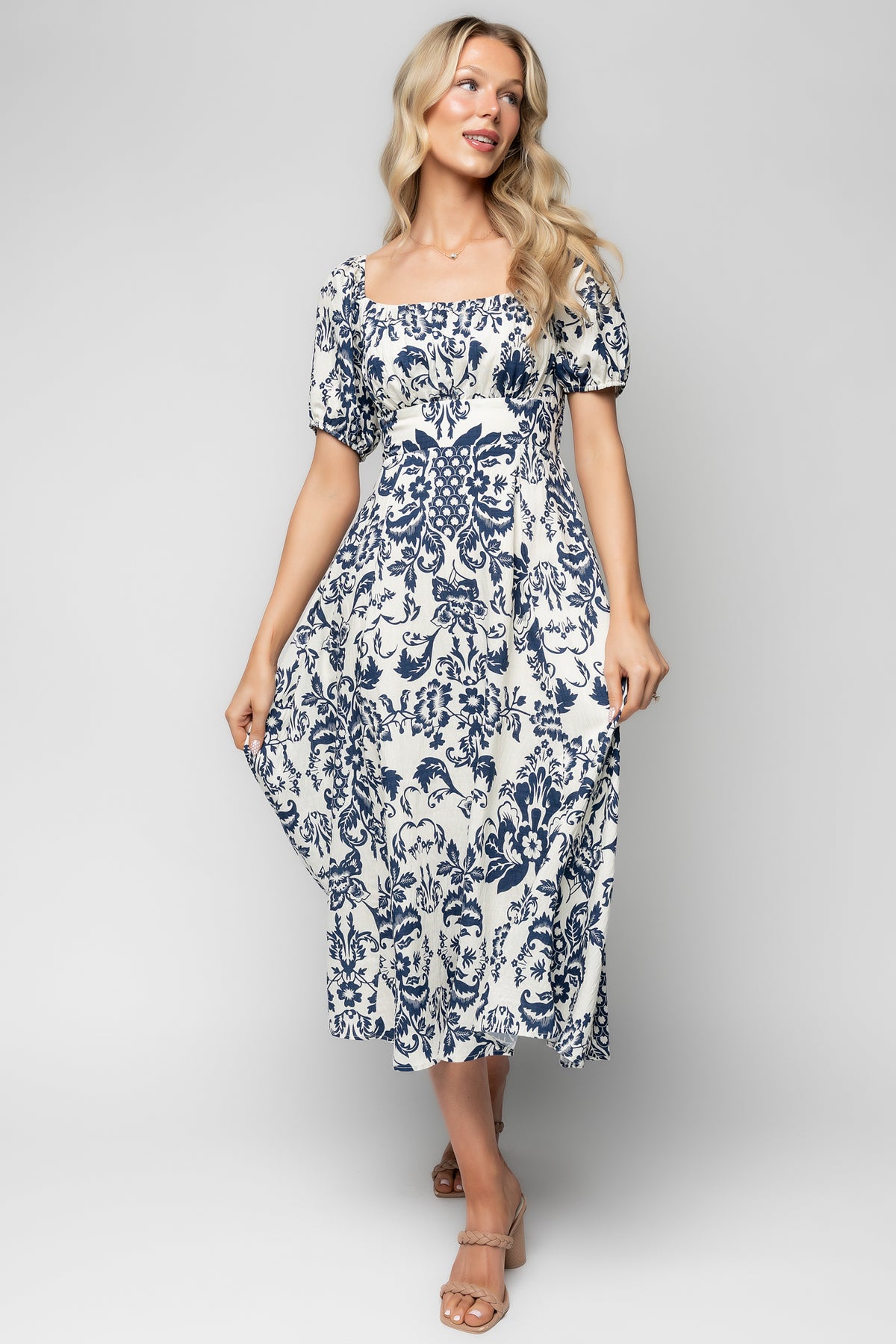 Full-length pose of the ivory and dark blue floral midi dress on model, highlighting banded waist, oversized sleeves, and soft drape of the fabric.