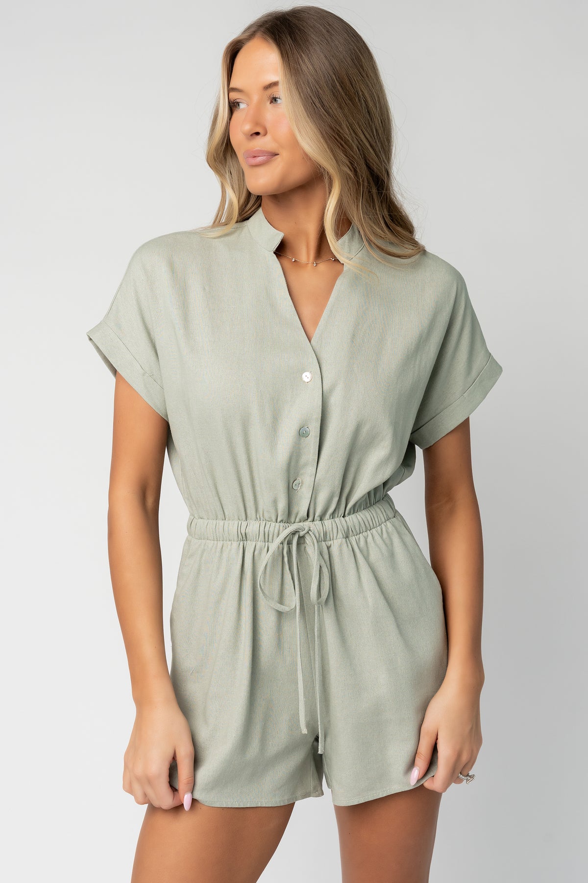Close-up of button-front detail and V-neckline on the light sage Winnie romper, highlighting the woven-like fabric texture and stitching.