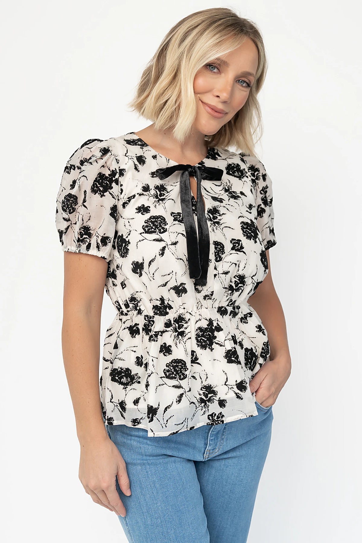 Gwenyth Peplum Blouse in Ivory + Black with velvet florals, front bow, puff sleeves, and elastic peplum waist.