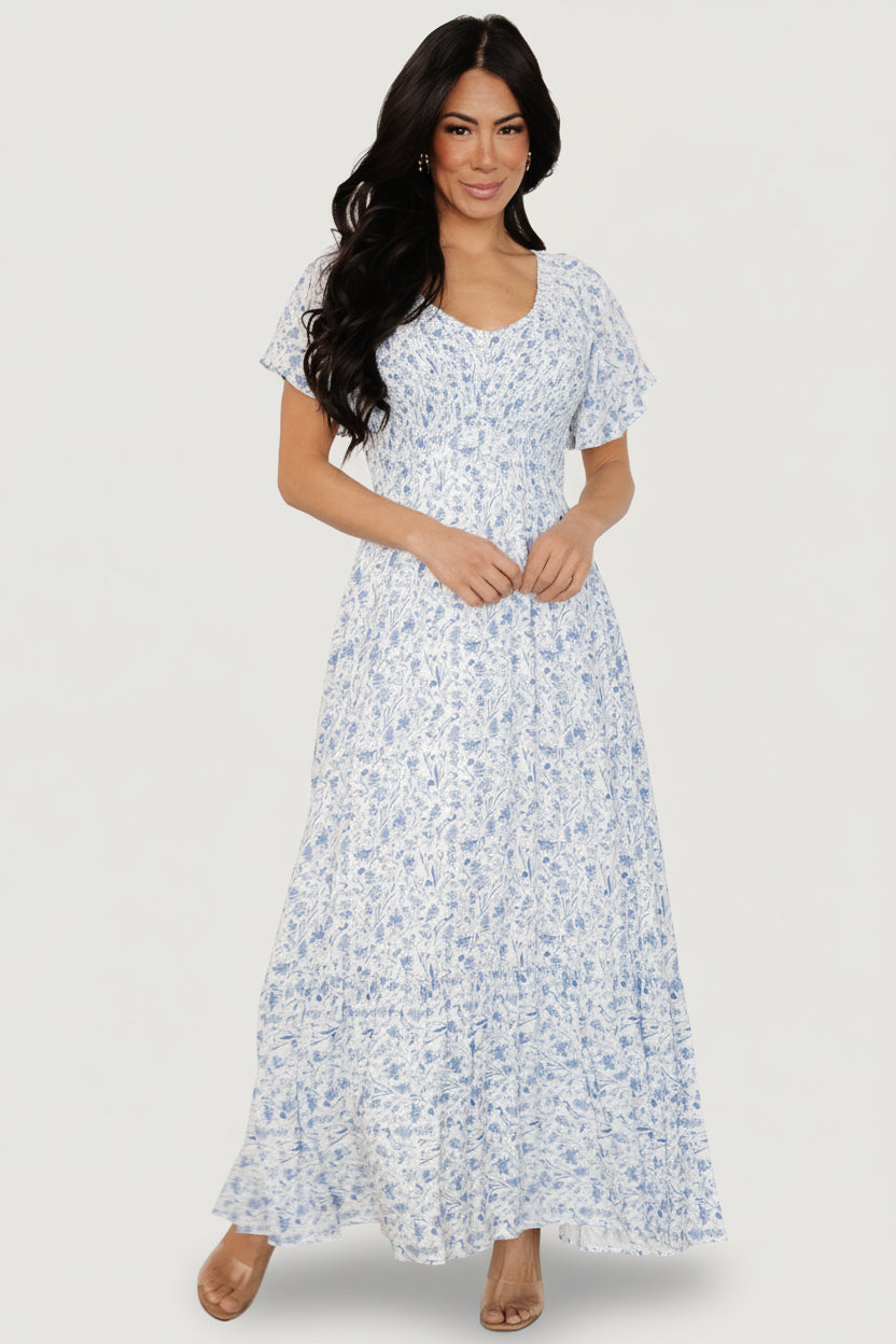 Back and side angle of the Joanie midi dress in white with blue floral, showing relaxed fit, skirt movement, and hemline length.