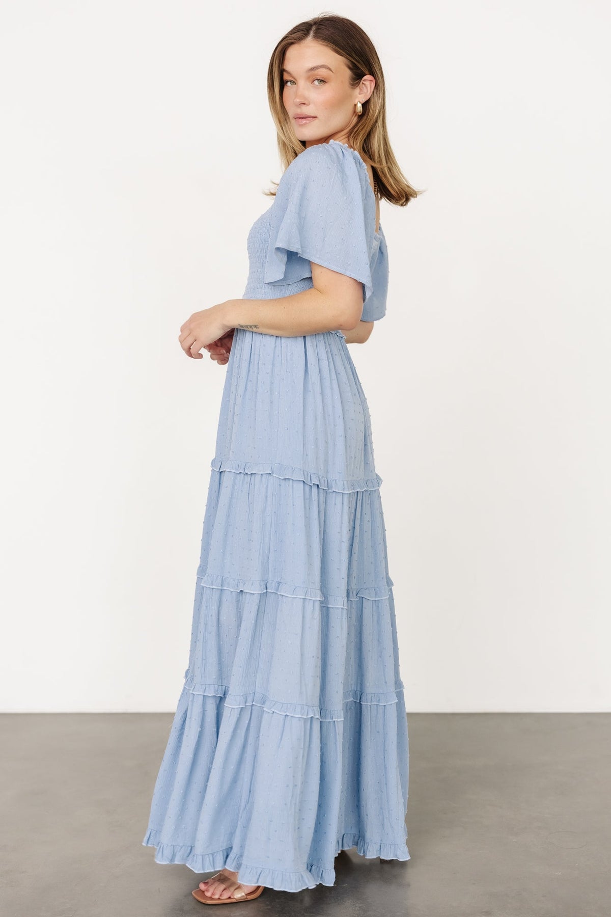 Styled flat-lay and detail shot of dusty blue Lenora maxi dress focusing on fabric texture, ruffle tiers, and lining information.