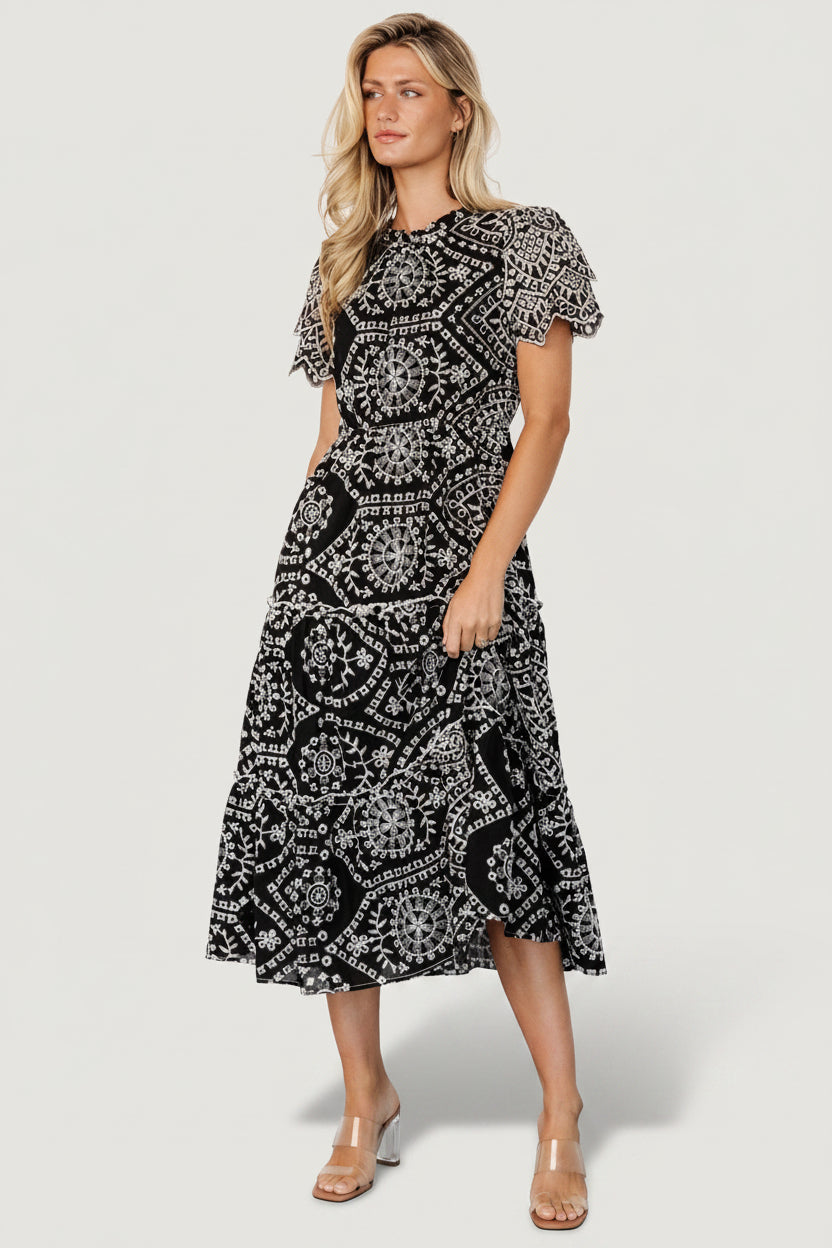 Model wearing Mirabel Eyelet Midi Dress in black and white, showing fit at waist, tiered skirt length and overall silhouette for styling.