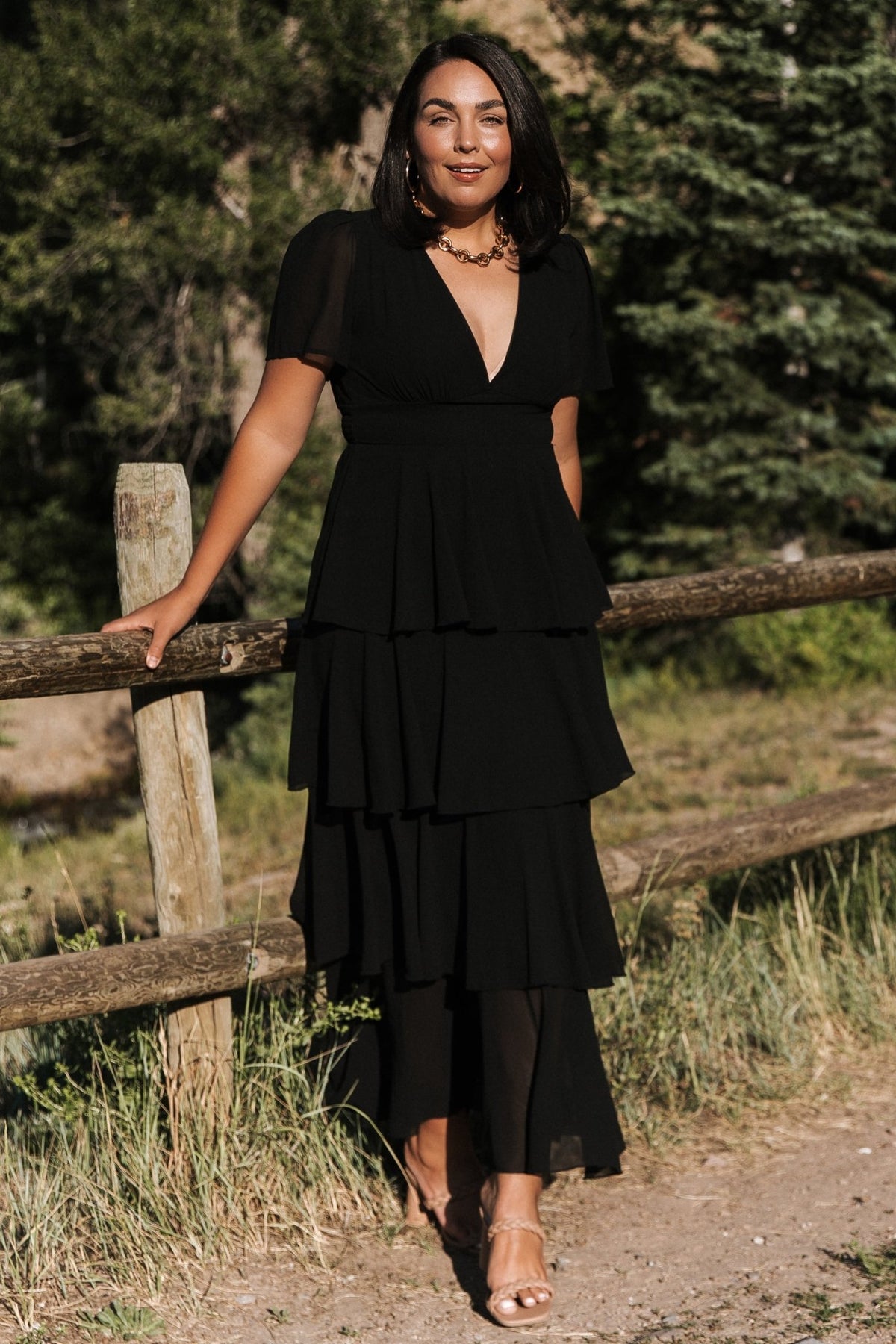 Front view of black Montaigne ruffle maxi dress on model showing plunging v-neck, short flutter sleeves, and cascading asymmetrical ruffle tiers.