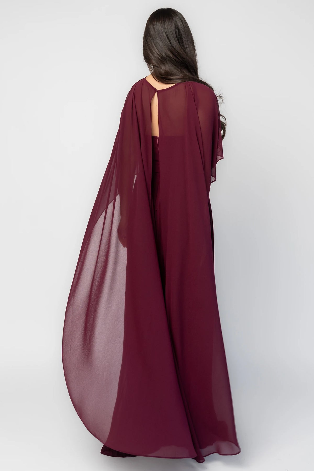 Serafina Strapless Gown in Burgundy with strapless neckline, removable sheer cape overlay, defined waist, and pleated skirt.