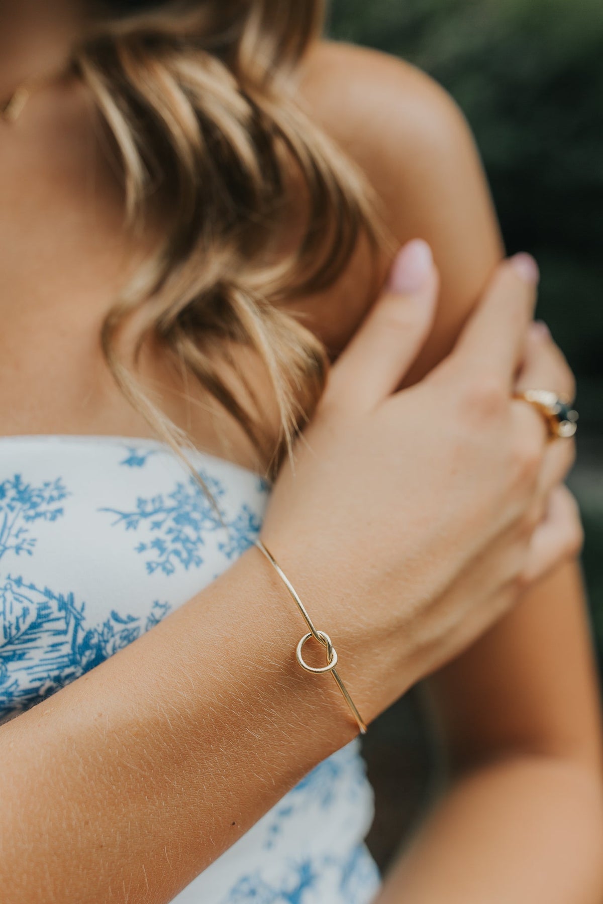 Close-up of The Kate Bangle knot detail in 18K gold plating over surgical-grade titanium, shown on a soft neutral surface for texture and finish.