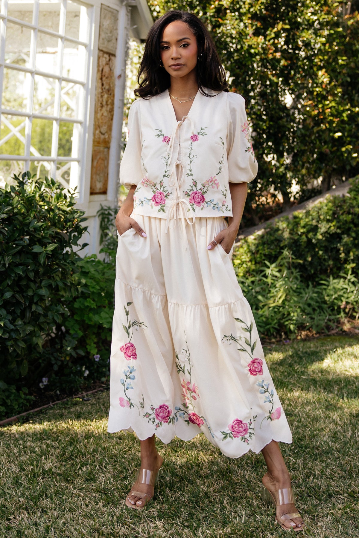 Close-up of multicolor pink, blue and green embroidery on cream fabric, highlighting stitch work and scalloped skirt edge.