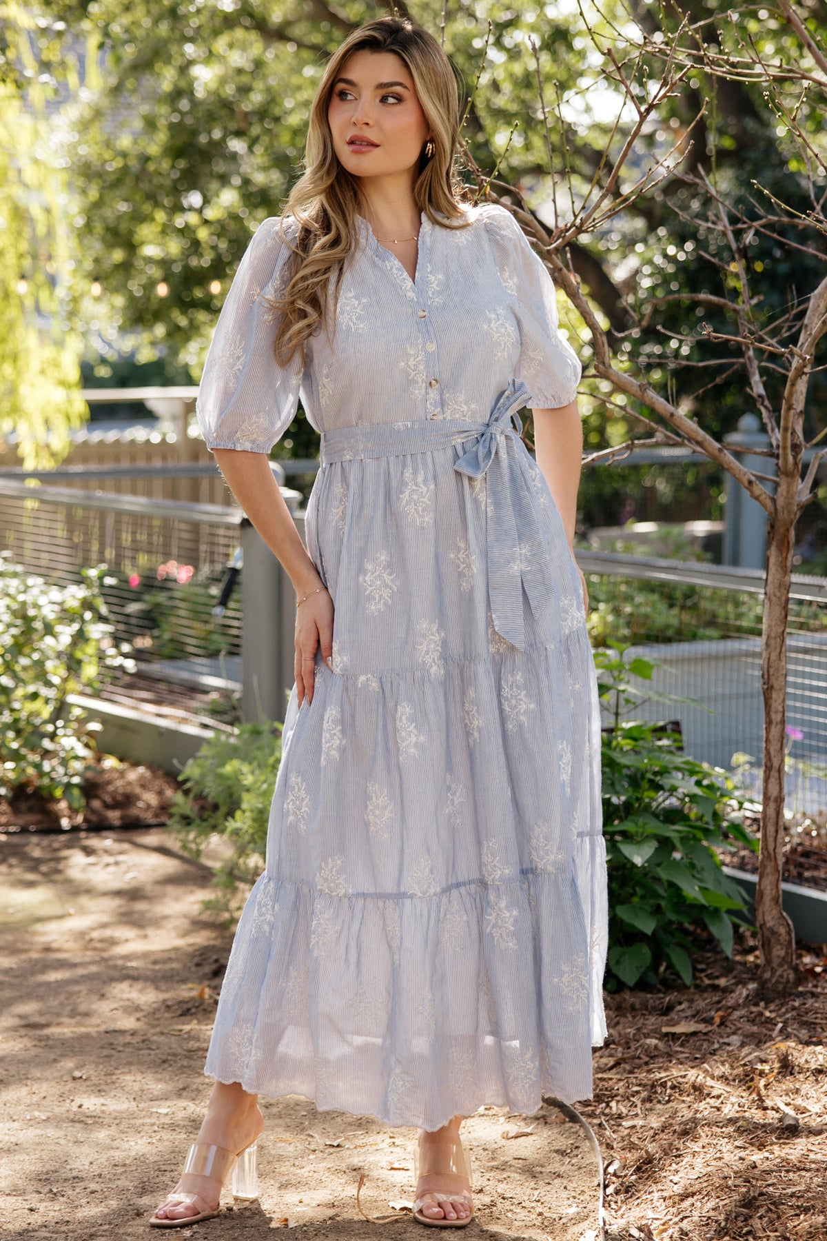 Front view of light blue Marguerite maxi dress with cream embroidered florals, V-neckline, removable waist tie, and functional side pockets.