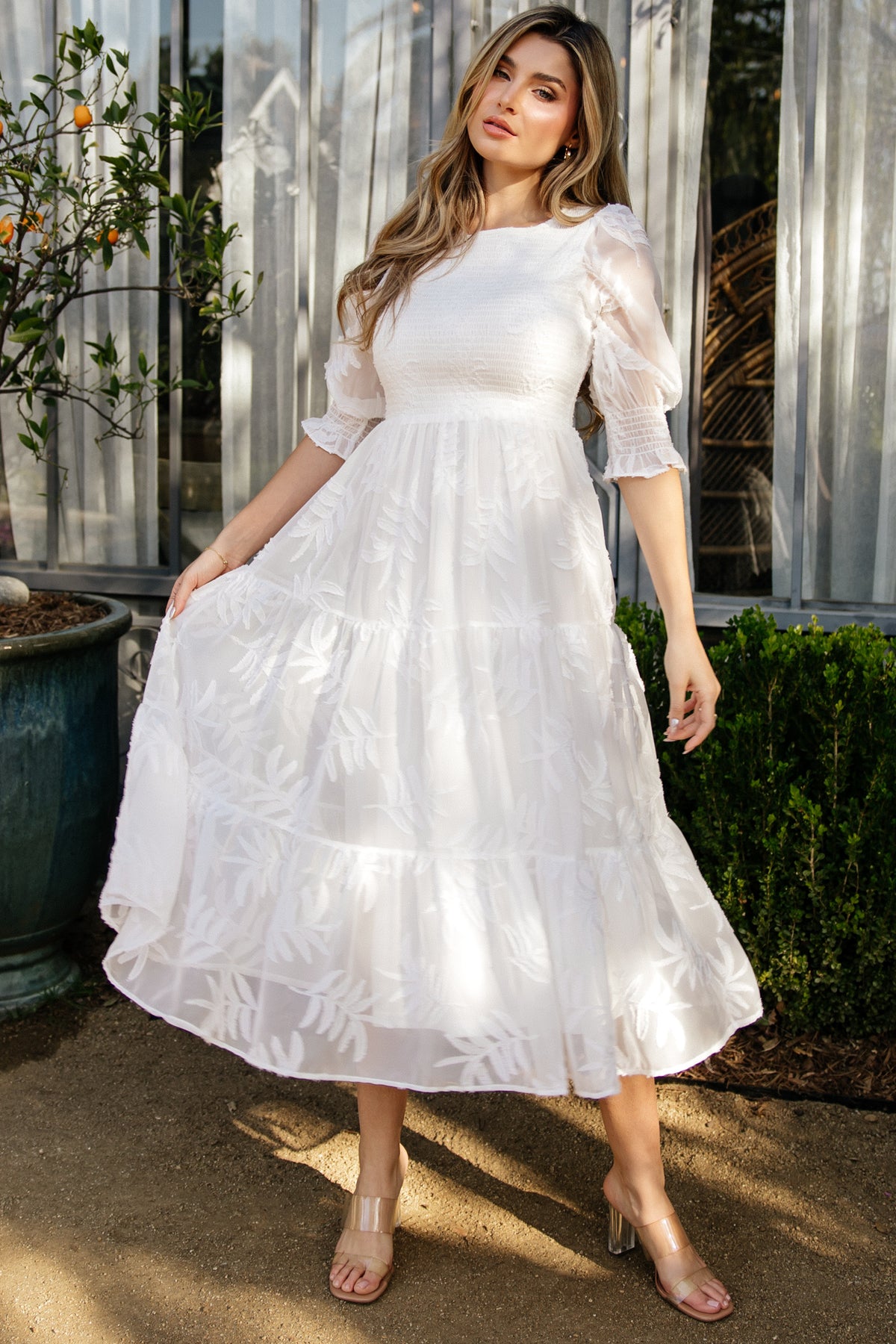 Front view of model wearing off-white Nellie Smocked Midi Dress with smocked bodice, puffed poet sleeves and three-tier chiffon skirt (100% polyester).