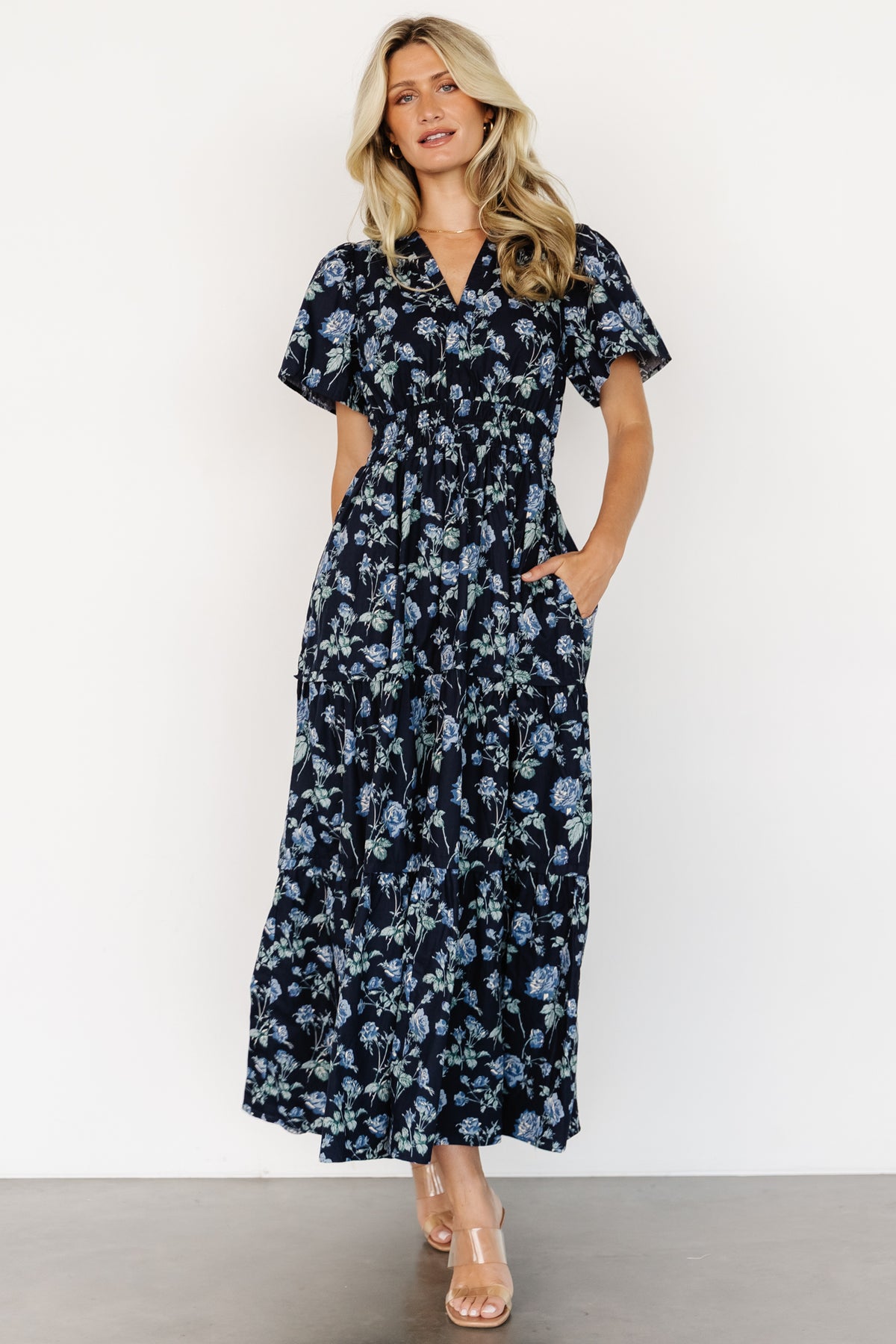 Front view of Kristin Maxi Dress in navy floral on model, showing notched V-neck, short sleeves, smocked waist and tiered skirt for movement.