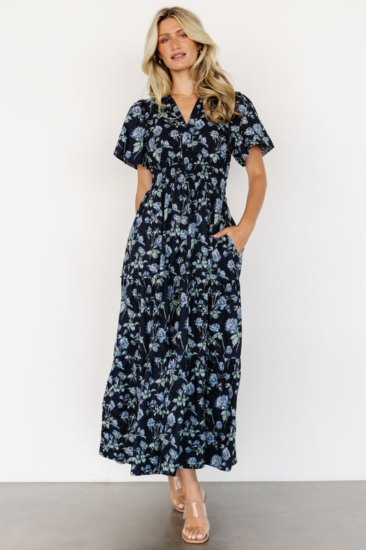 Front view of Kristin Maxi Dress in navy floral on model, showing notched V-neck, short sleeves, smocked waist and tiered skirt for movement.