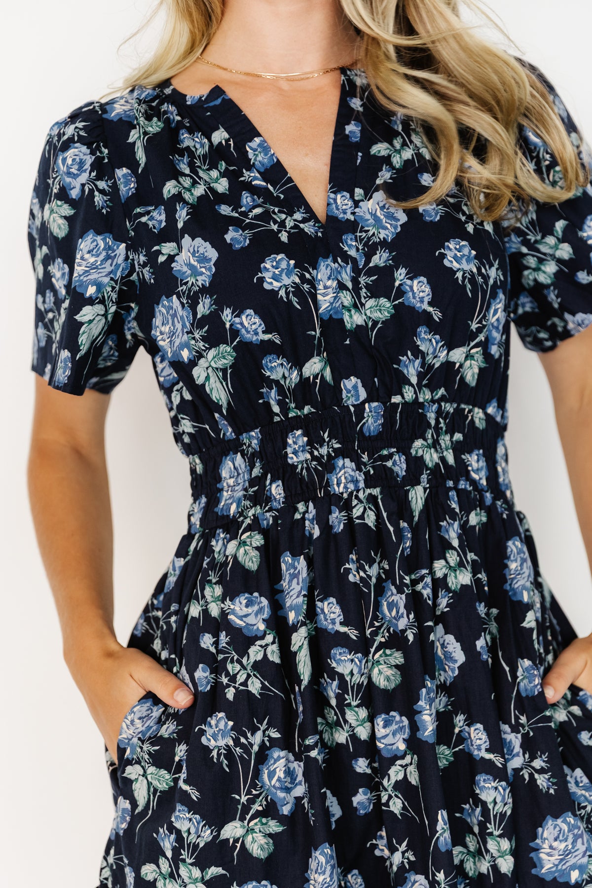 Three-quarter view of navy floral Kristin Maxi Dress on model, highlighting smocked waistband, short sleeves and flowing tiered maxi silhouette.