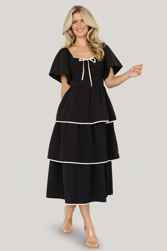 Front view of the Madrid Tiered Midi Dress in black with ivory trim, showing the sweetheart neckline and small decorative bow detail.