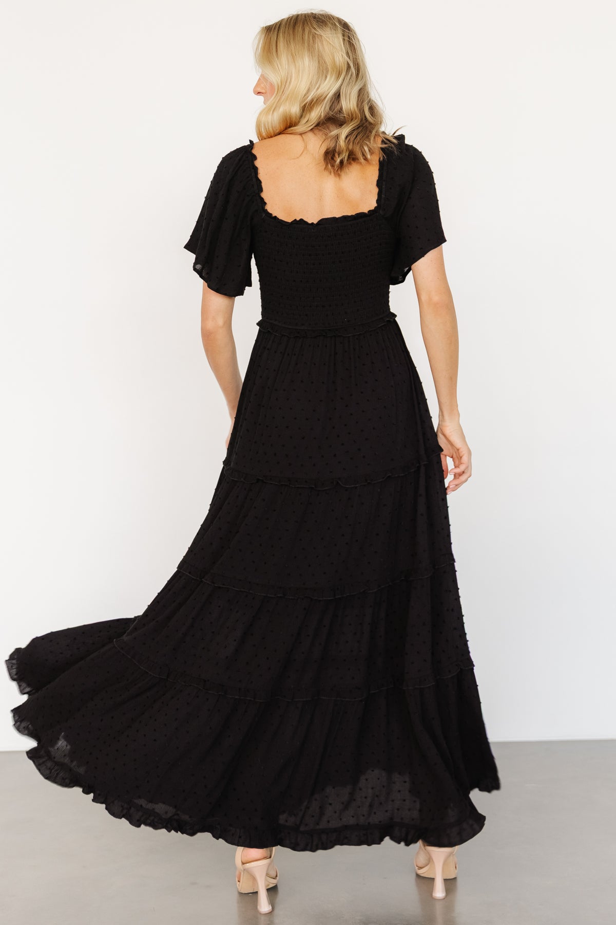 Full-length shot of Lenora smocked dotted maxi dress in black, showing tiered ruffle skirt movement and overall silhouette on a standing model.