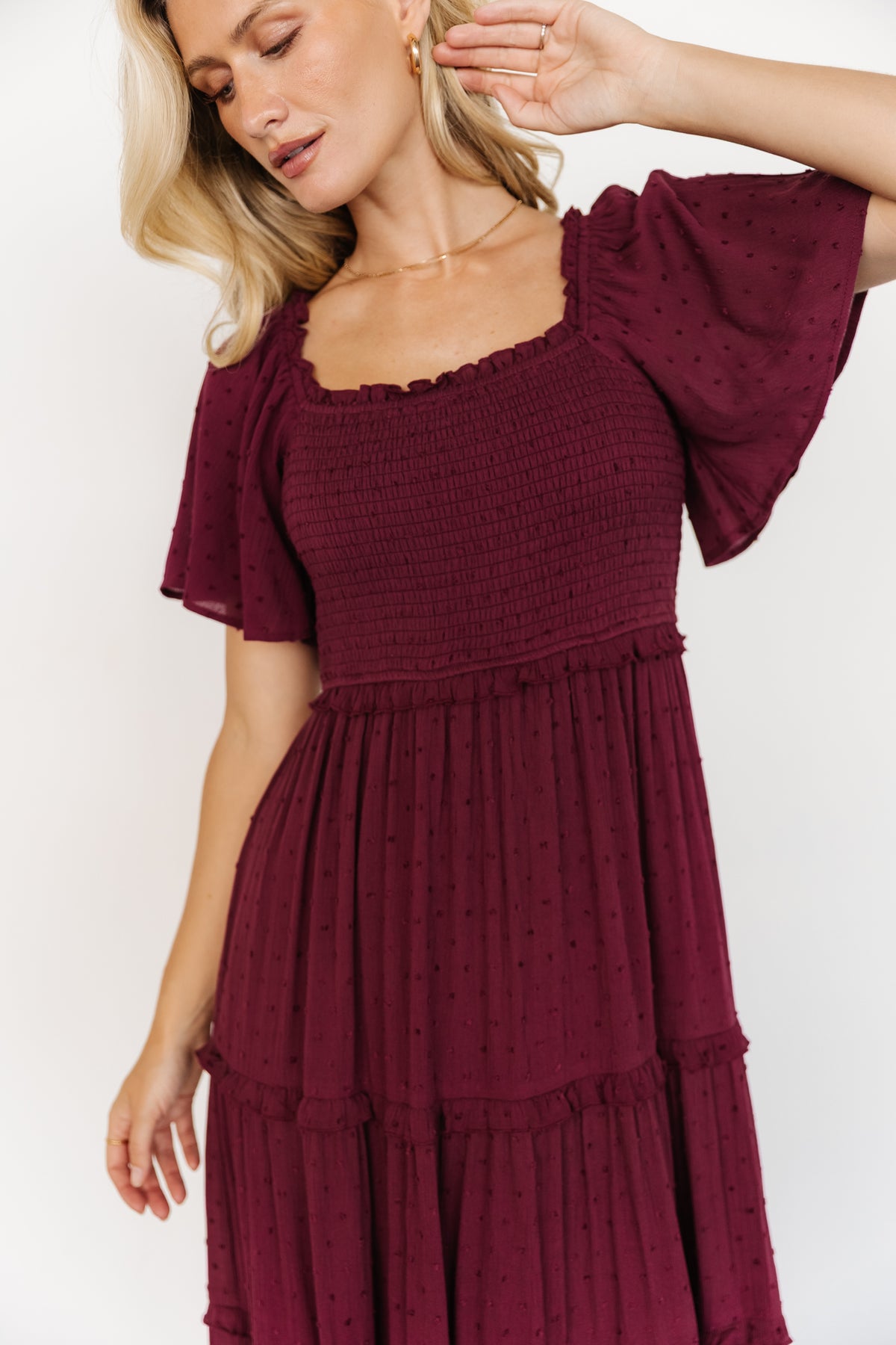 Three-quarter shot of wine Lenora maxi dress on model, highlighting ruffled elastic waist and flowing tiered skirt movement.