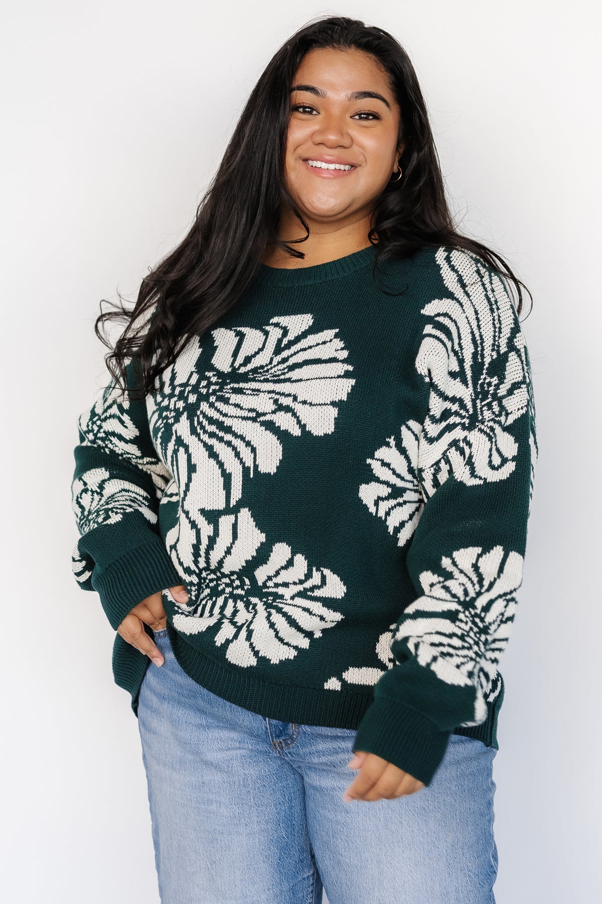 Model wearing Maude sweater in an everyday setting, showing overall length, relaxed hemline and the scale of the off-white floral print on green knit.