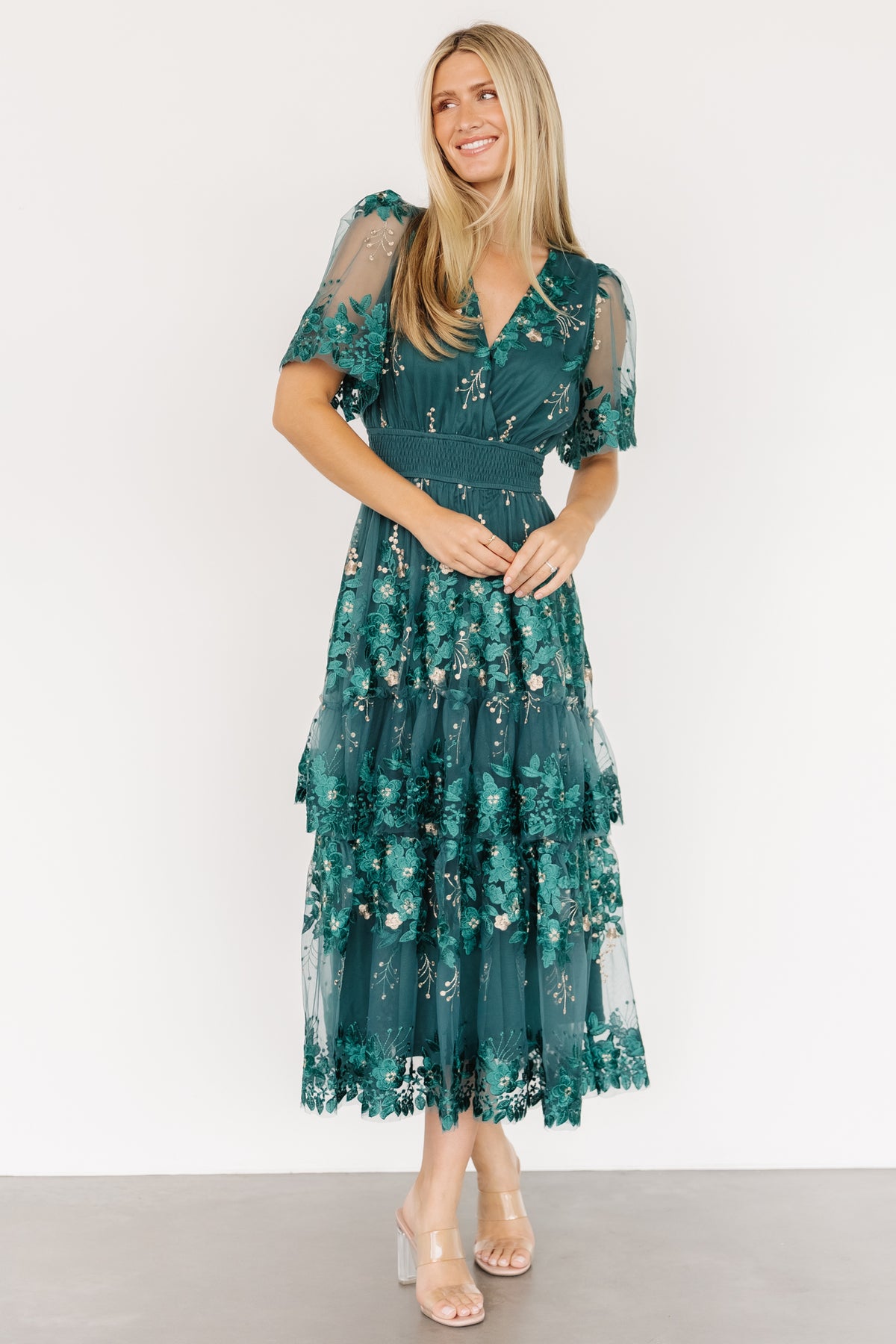 Model wearing Lotte dress in emerald, full-length view highlighting midi hem, tiered ruffle overlay and soft tulle movement as she poses.
