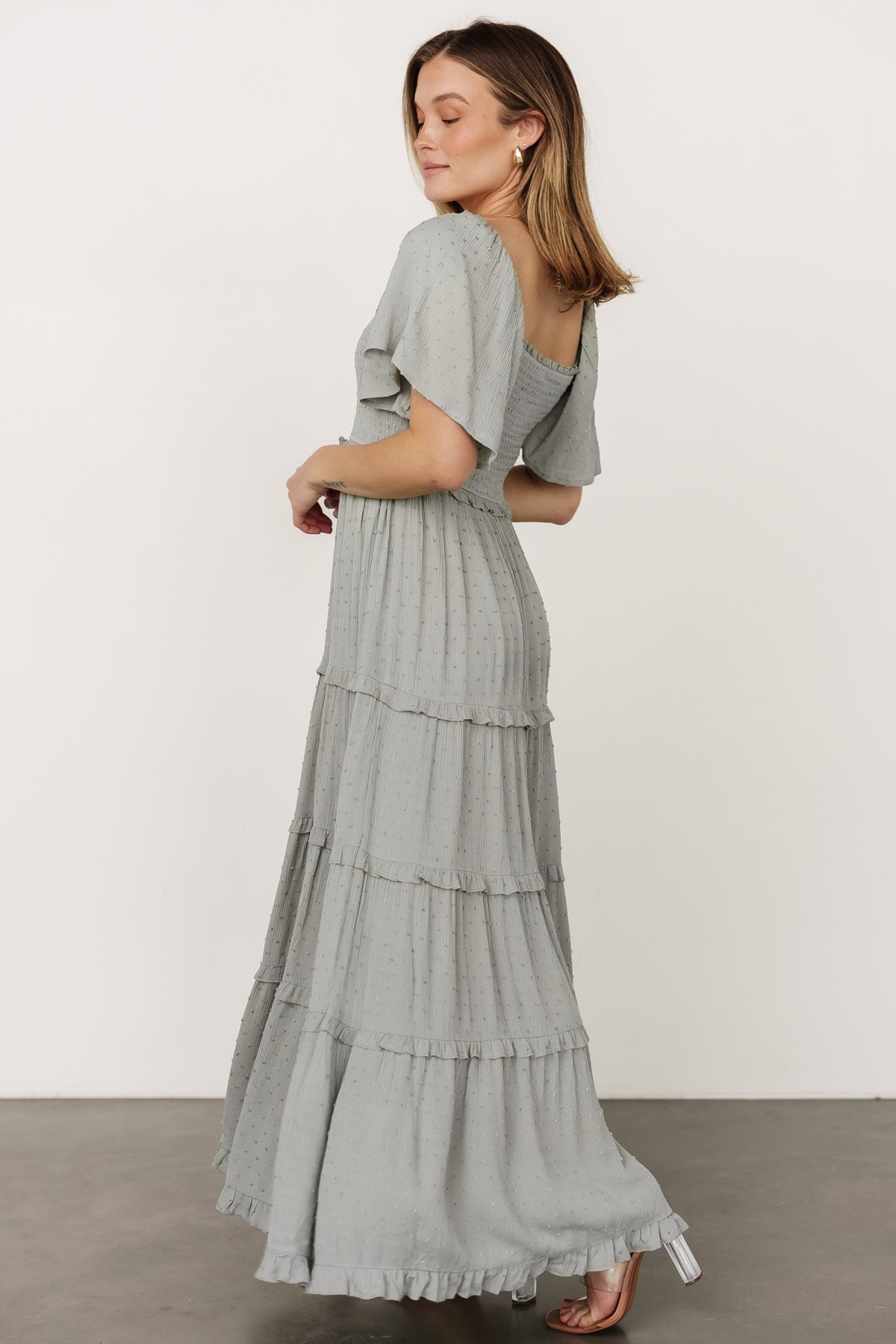 Full-length portrait of model in Lenora maxi dress in sage, styled with simple jewelry to emphasize silhouette, smocking, and tiered skirt.