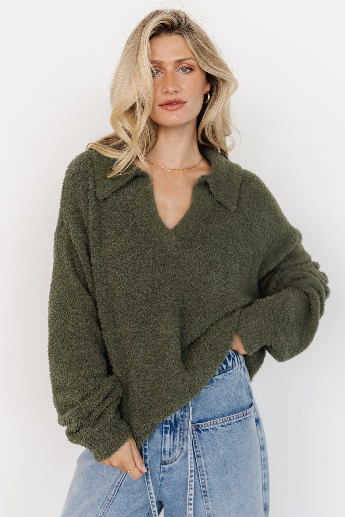 Side-angle of Lockwood sweater on model emphasizing relaxed silhouette, collared V-neck and sleeve length in muted green.