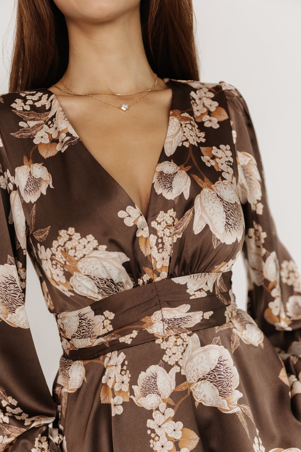 Close-up of the dress bodice showing V-neckline, smocked back detail and smooth satin texture with multi-tonal mocha floral print.