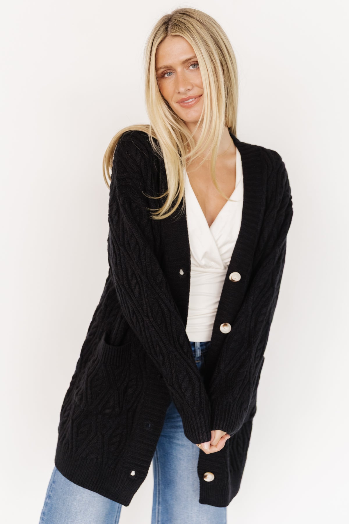 Styled flat-lay of the Alberta Cable Knit Cardigan in black, showing the five-button front, chunky cables, and wide ribbed hem and placket.