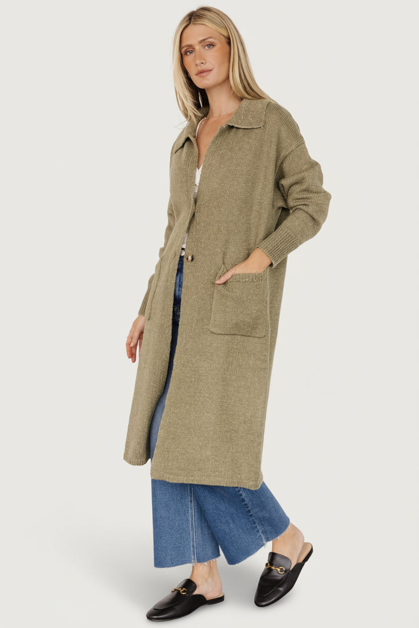 Styled outfit shot with heathered olive cardigan over jeans, showing longline silhouette and small ribbed bottom hem.