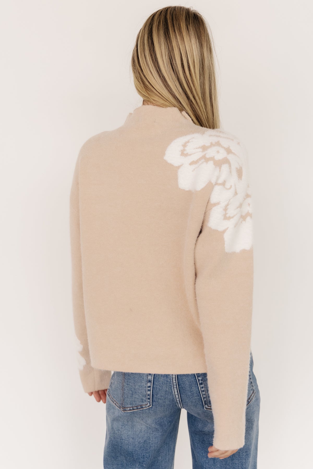 Detail of left sleeve cuff with embroidered accent flower and close-up of the wide knit texture at the hem and cuff.