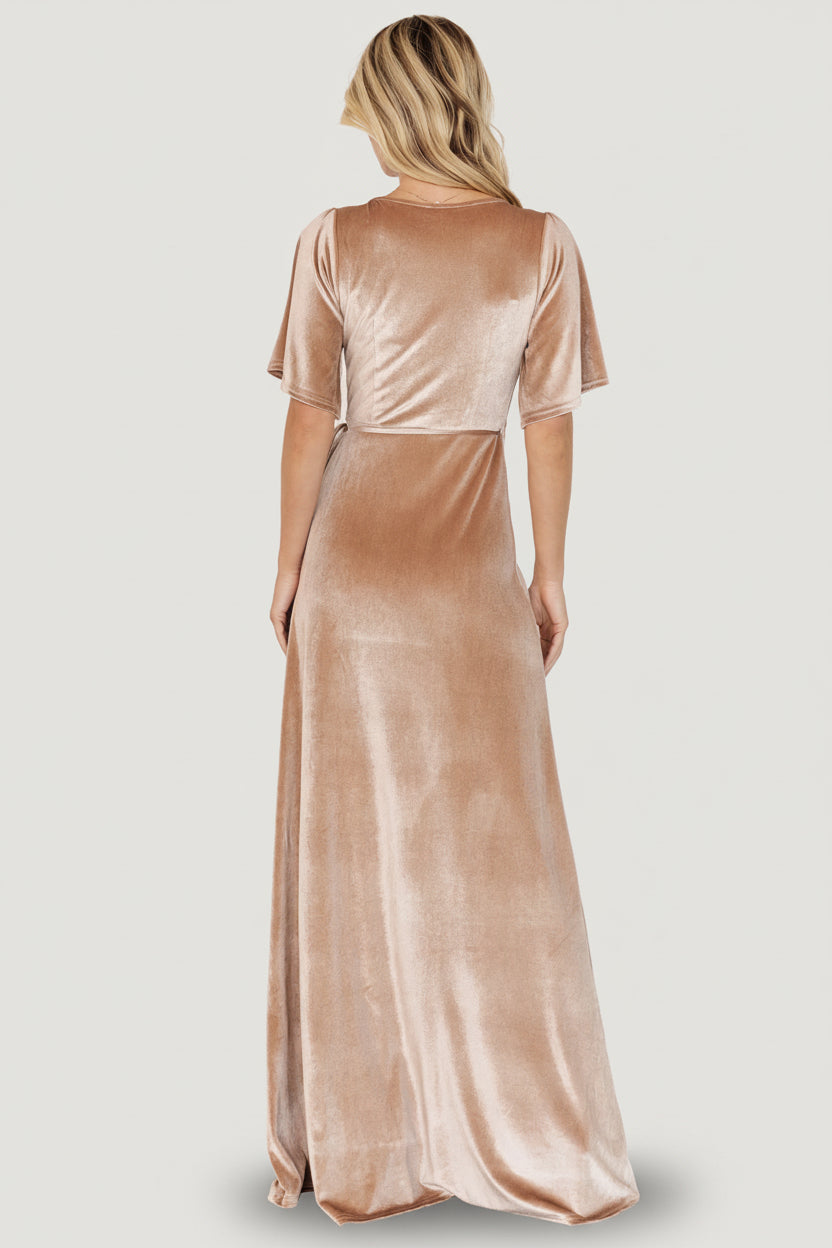 Side view of model wearing the champagne velvet wrap dress, illustrating sleeve length, tulip hem movement, and how the waist tie sculpts the silhouette.