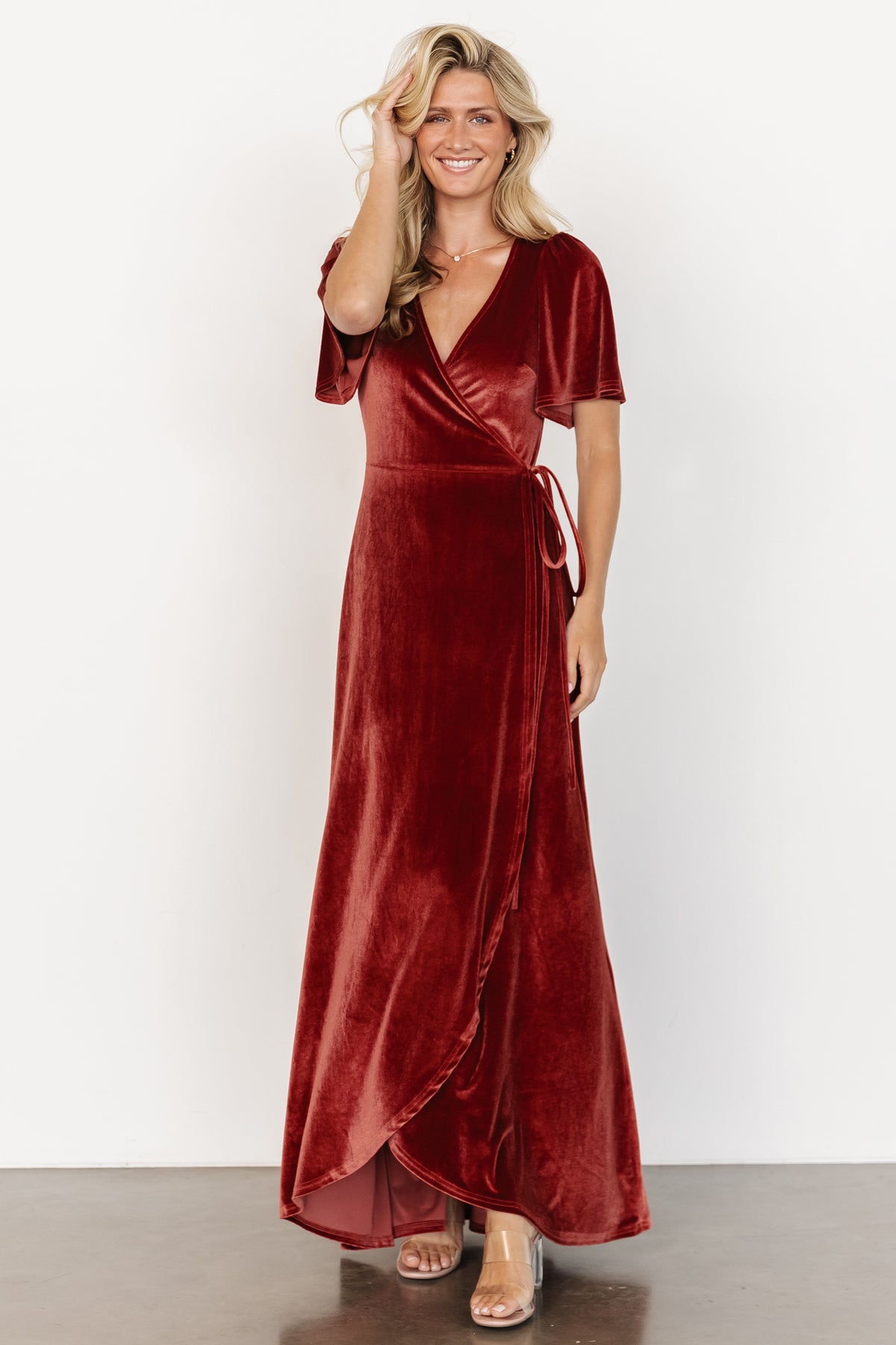 Full-length side view showing terracotta velvet wrap dress movement and tulip skirt, highlighting the drape and subtle stretch of fabric.