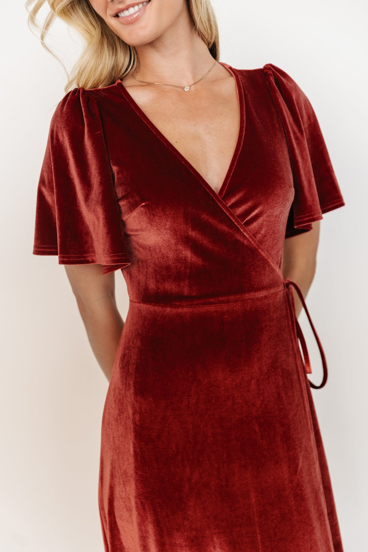 Movement shot of terracotta velvet wrap dress walking, showing tulip skirt opening and elegant drape for occasion wear.