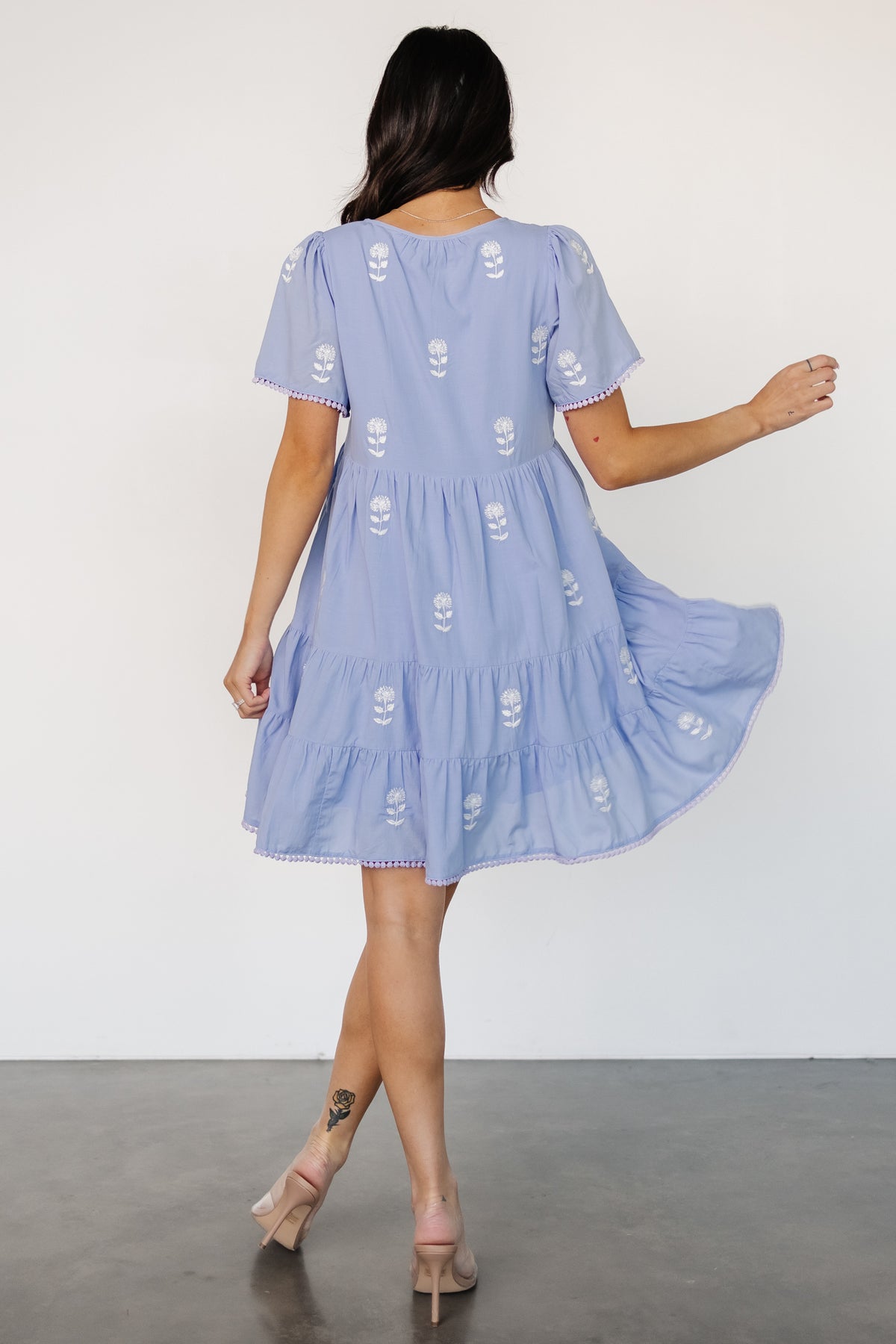 Side view highlighting hidden side pocket and left-side zipper on short tassel hem dress with embroidered floral motif.