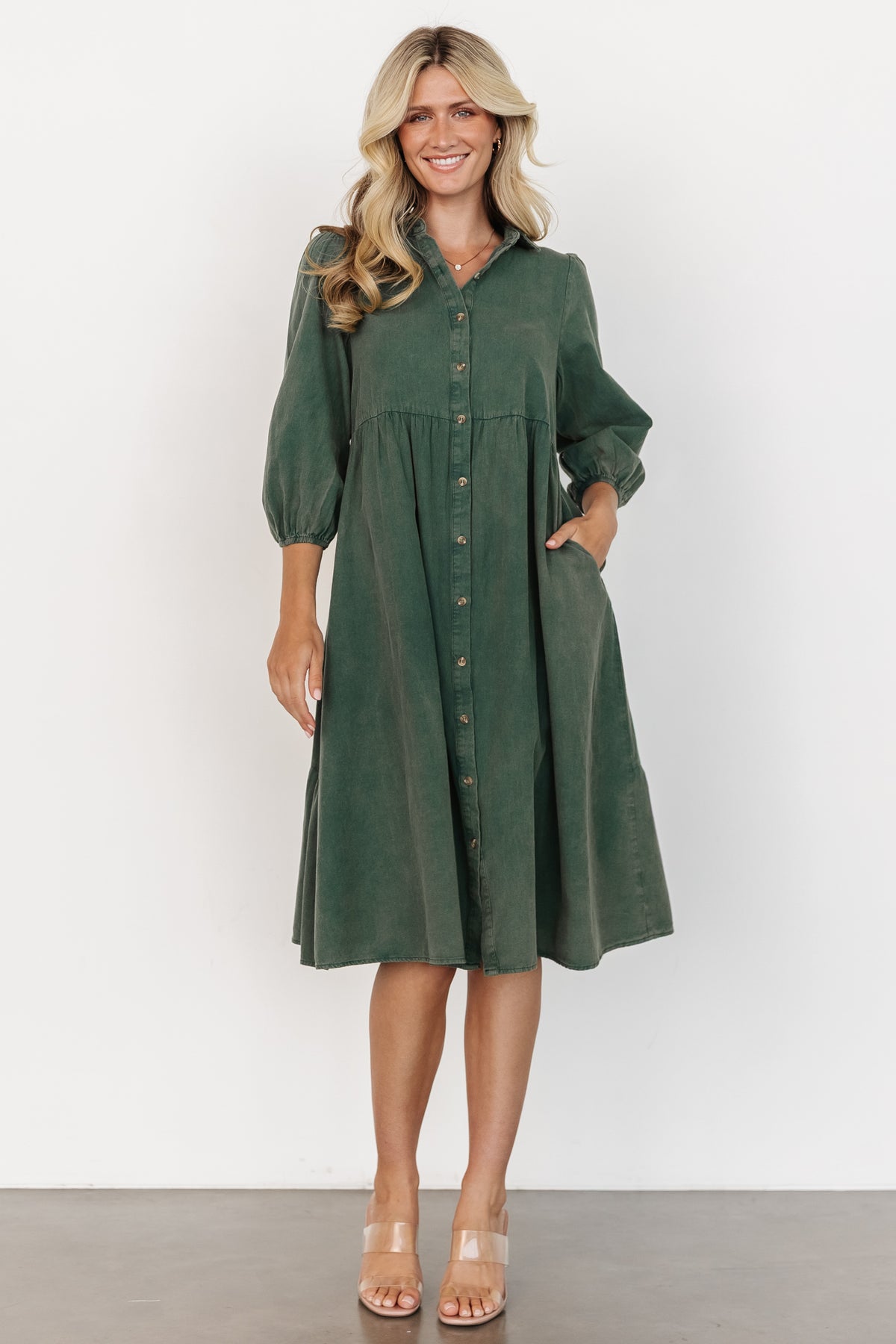 Front view of model wearing forest green Sari Babydoll Dress showing button-front collar, gathered tiers, 3/4 sleeves, and side pockets.