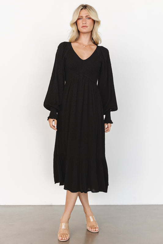 Front view of Lainey smocked dotted midi dress in black on model, showing V-neck, smocked bodice, long sleeves, and tiered hem for a soft drape.