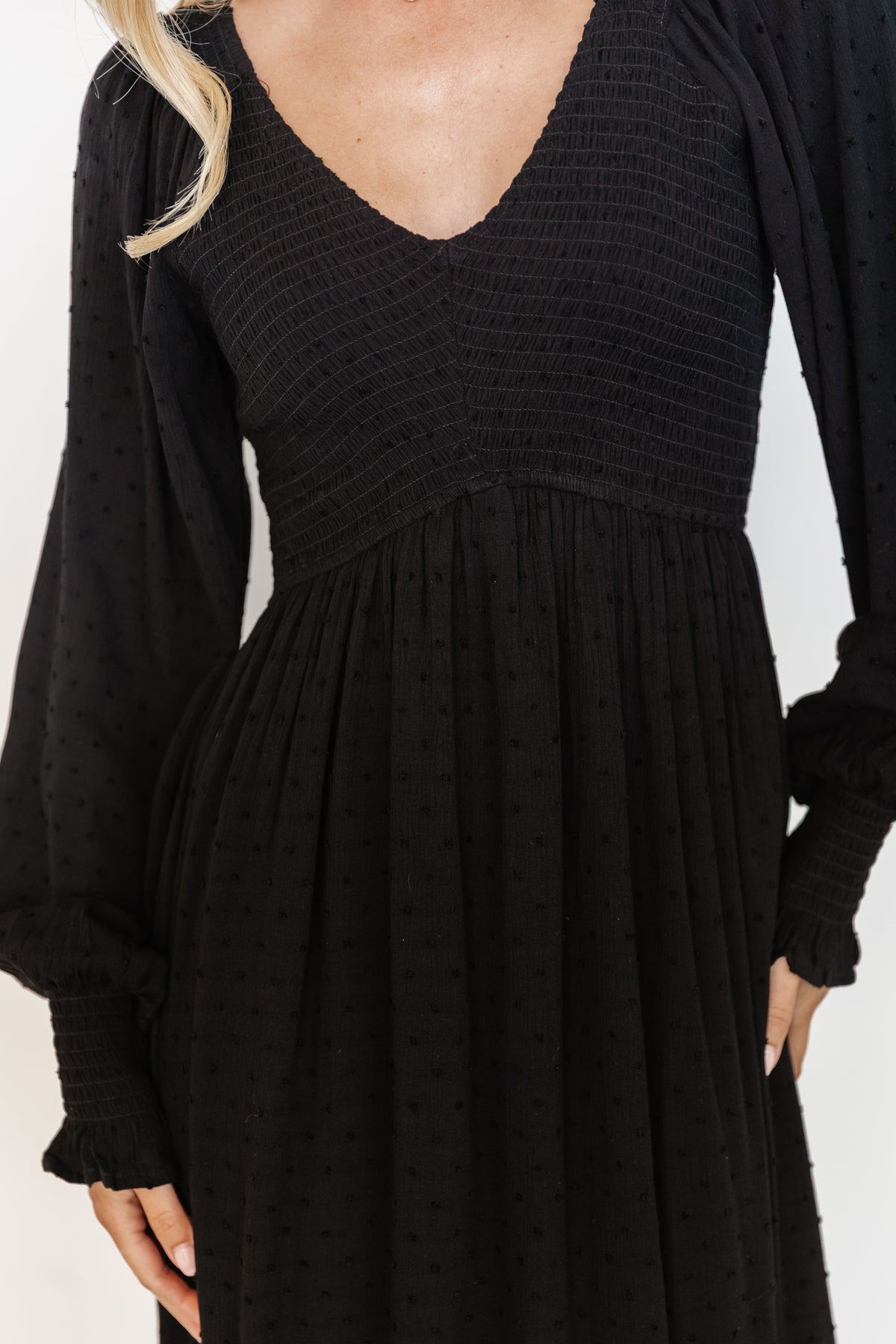 Side view of black Lainey smocked midi dress on model, highlighting the dotted textured rayon, elastic waist, and flowing tiered skirt movement.