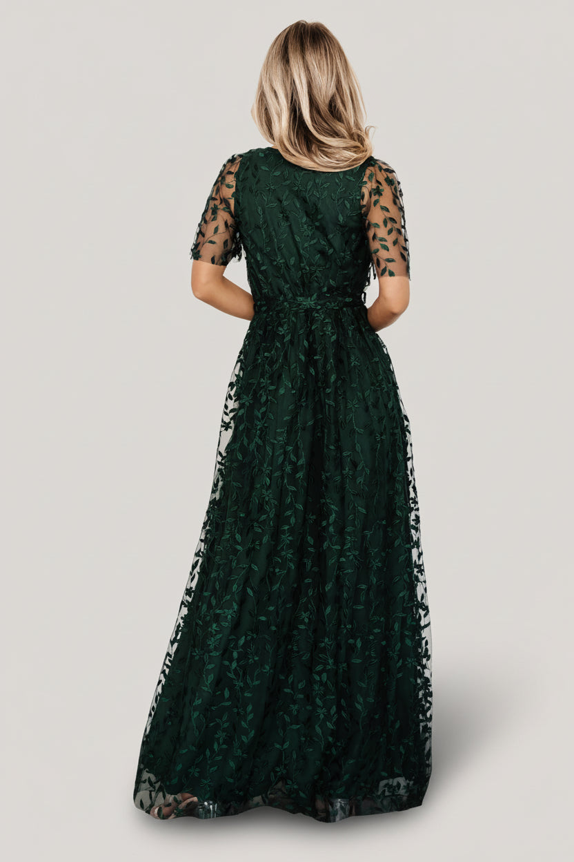 Three-quarter model shot showing short unlined sleeves and textured vine embossing on dark green organza fabric, highlighting sleeve detail.
