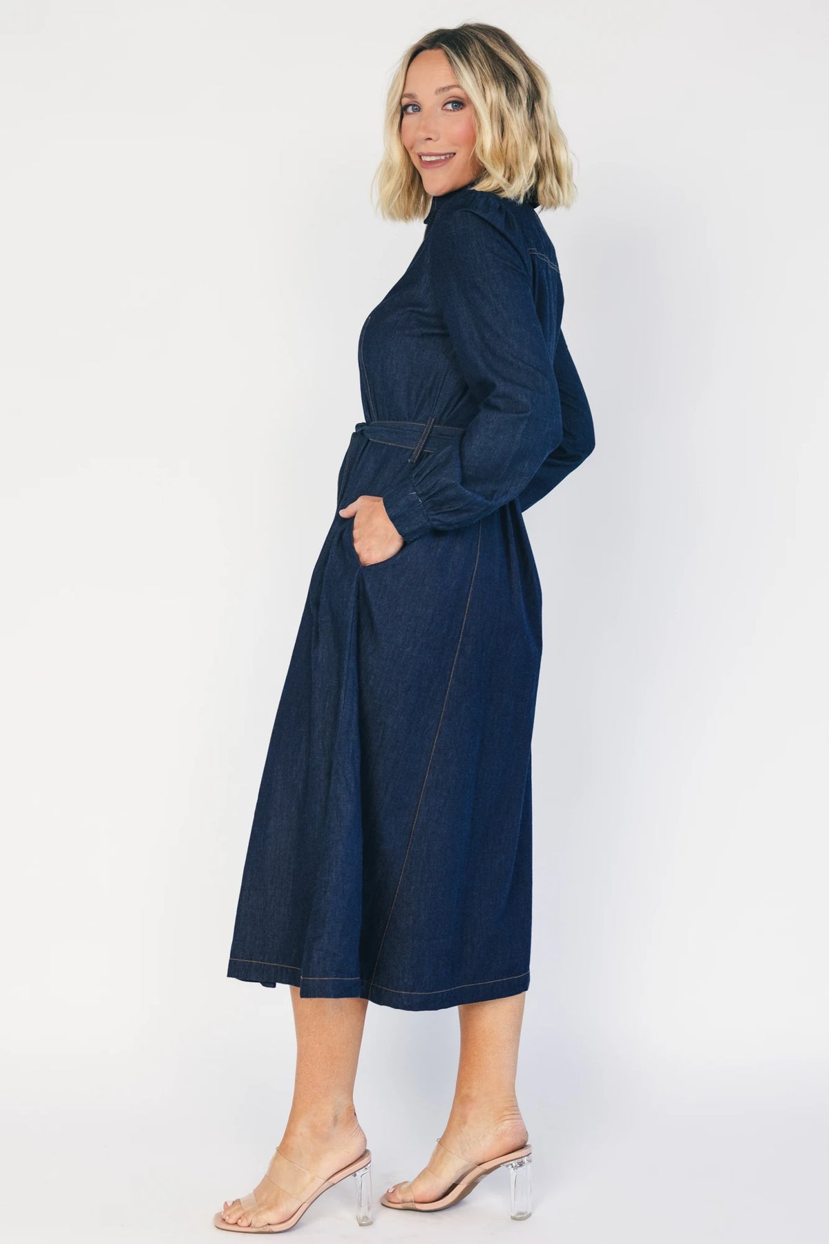 Model wearing a dark chambray midi shirtdress with a collared neckline, half-zip front, long sleeves, and a removable waist sash.
