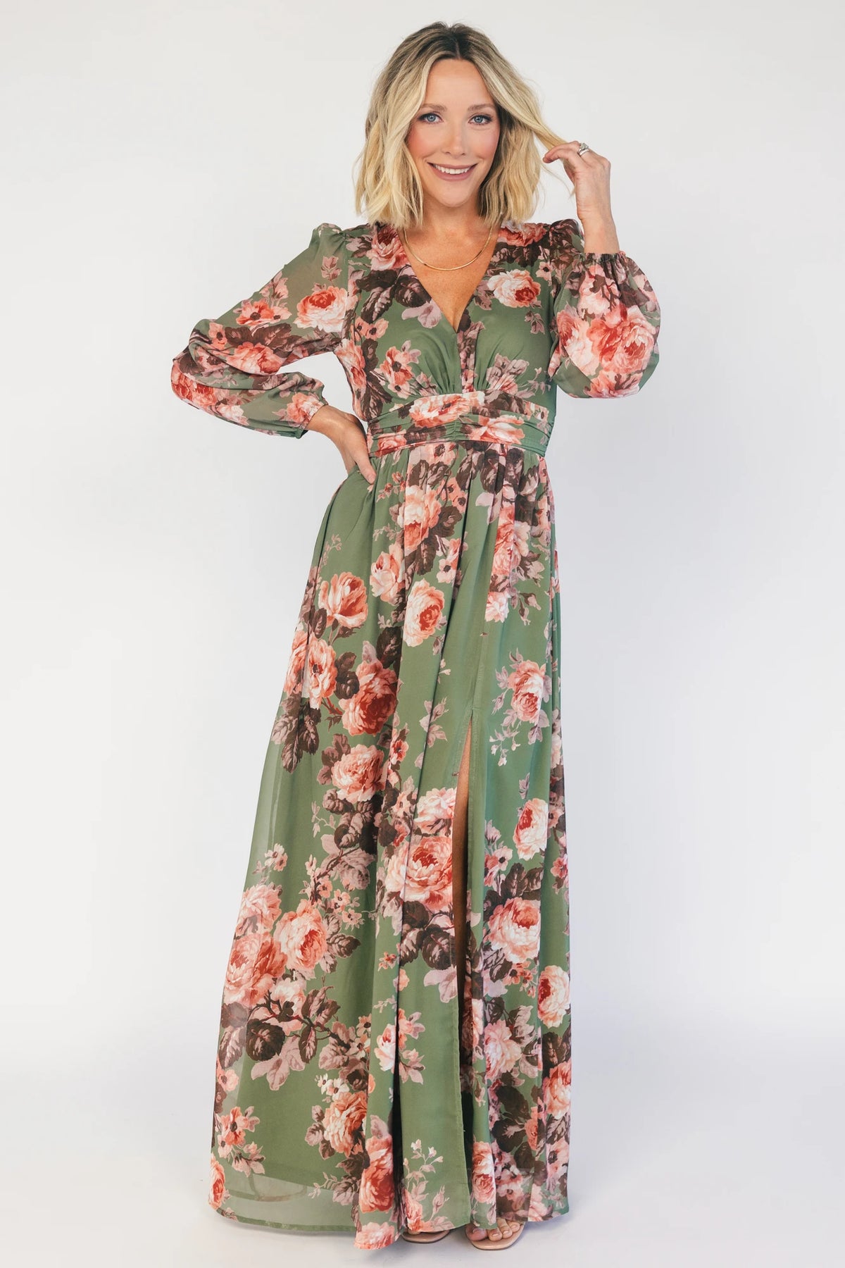 Model wearing a green floral maxi dress with a V-neckline, long bishop sleeves, and a gathered waist with a smocked back.
