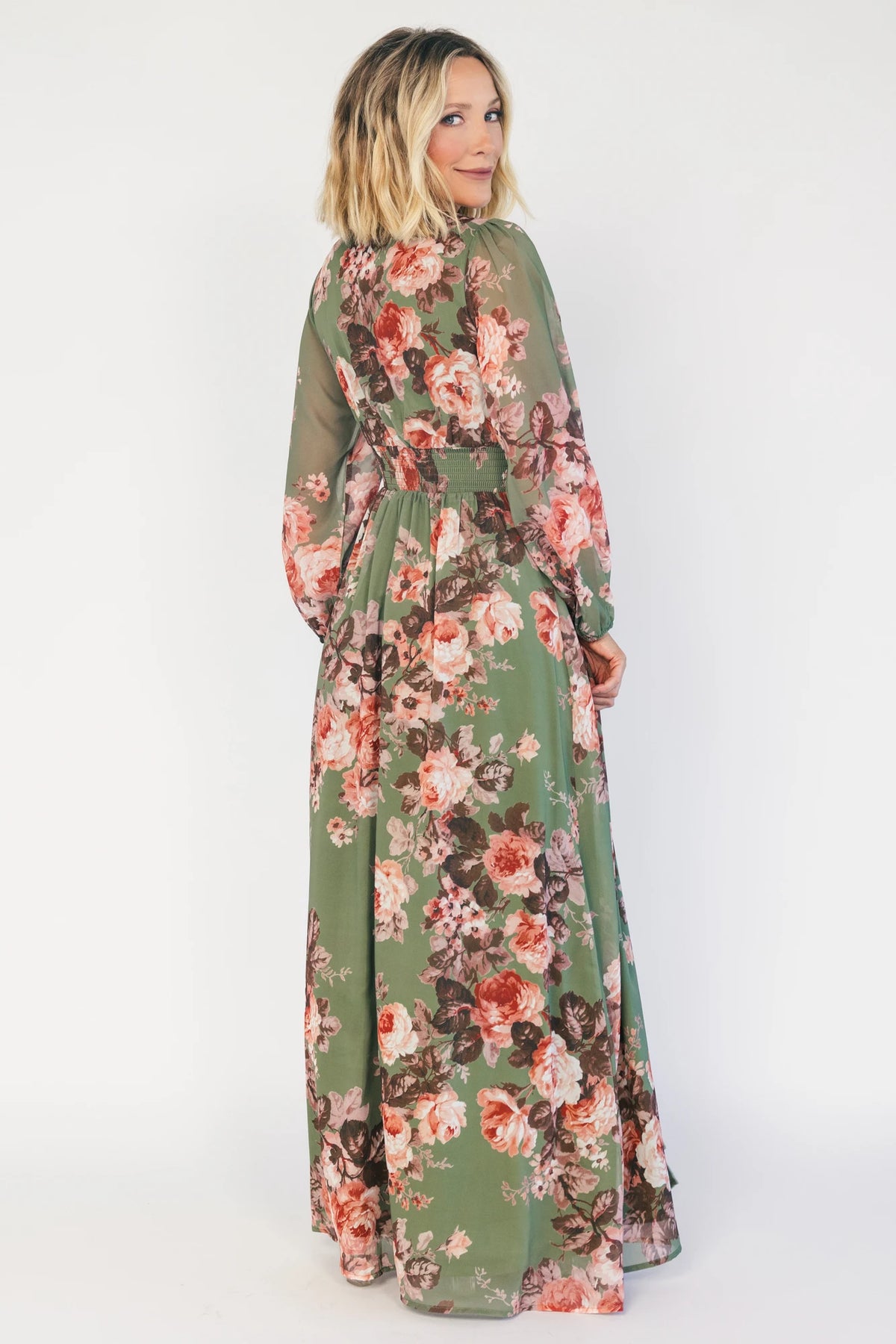 Model wearing a green floral maxi dress with a V-neckline, long bishop sleeves, and a gathered waist with a smocked back.